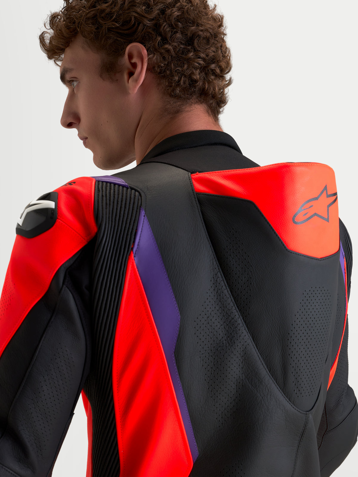 Alpinestars Missile V3 Leather Suit 1 Piece, mono de moto de cuero para hombre, negro, rojo flúor y morado, joroba aerodinámica ventilada y protecciones DFS en los hombros, vista trasera y de hombro en modelo