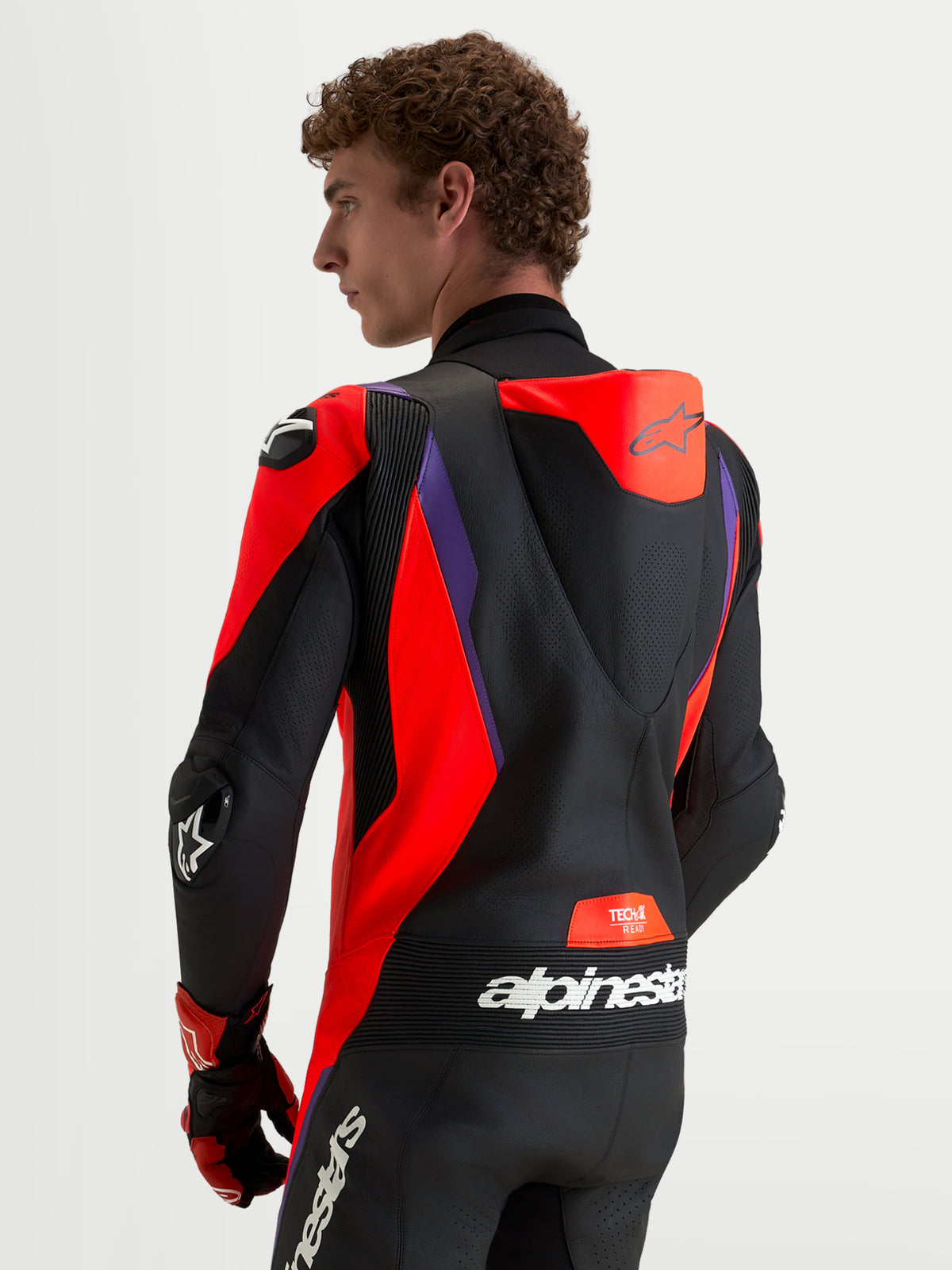 Mono de cuero Alpinestars Missile V3 de 1 pieza, mono de moto para carreras en negro, rojo y morado, con joroba aerodinámica ventilada y paneles elásticos de acordeón, vista trasera en modelo