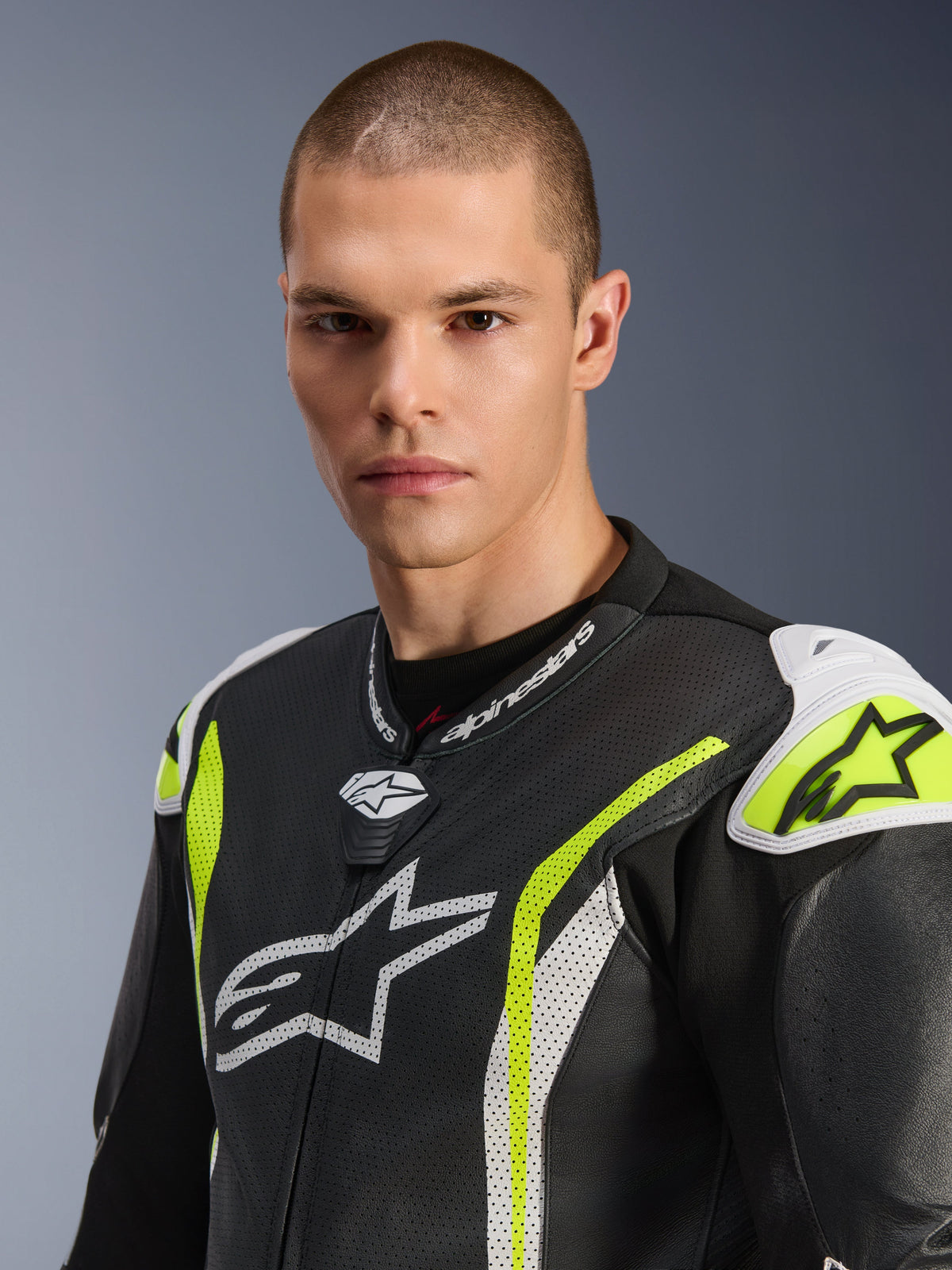 Primer plano de un modelo masculino luciendo el traje de cuero de una pieza Alpinestars GP Tech V5, negro, blanco y amarillo flúor, con cuero perforado, logotipos de Alpinestars blancos en el pecho y los hombros, y acentos en amarillo vibrante, equipamiento profesional de carreras.