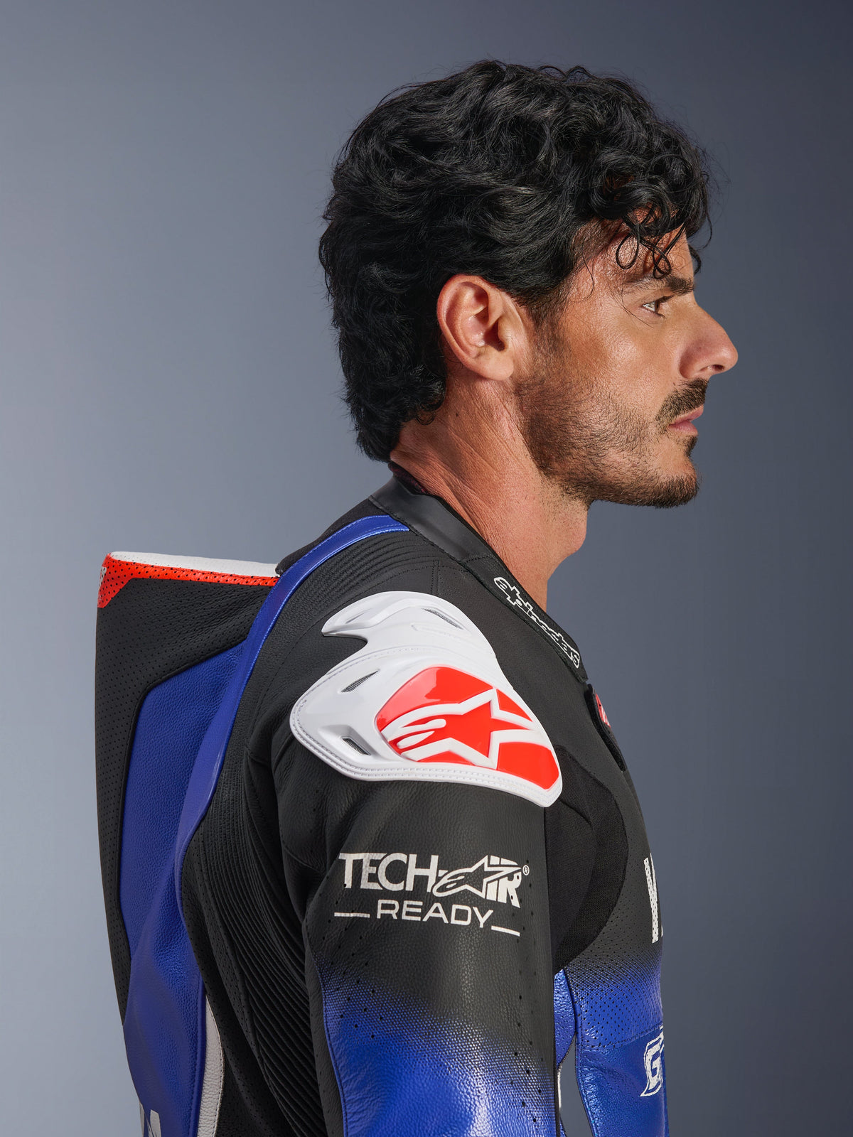 Mono de cuero de una pieza Yamaha GP-R7 de Alpinestars, azul metálico y negro con detalles en blanco y rojo, perfil lateral que destaca la joroba aerodinámica, protección de hombro blanca con el logo de Alpinestars en rojo, marca Tech-Air Ready en la manga y cuero de competición perforado de primera calidad.
