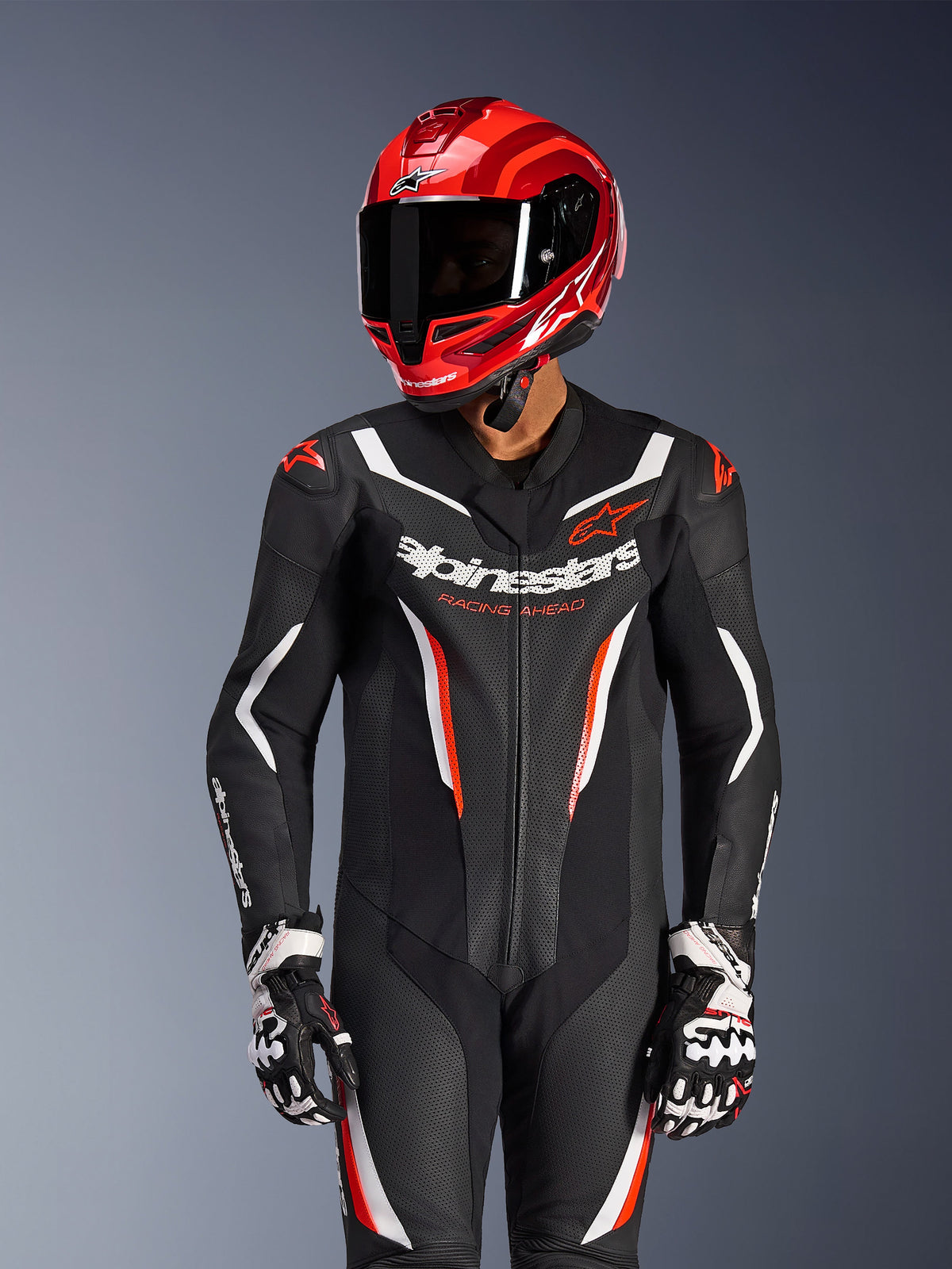 Piloto de motociclismo con traje de cuero de una pieza Alpinestars GP Force V2 en Negro Blanco Rojo Fluo, casco y guantes de carreras rojos a juego, con paneles de cuero perforado y logotipos llamativos, equipo de carreras de alto rendimiento
