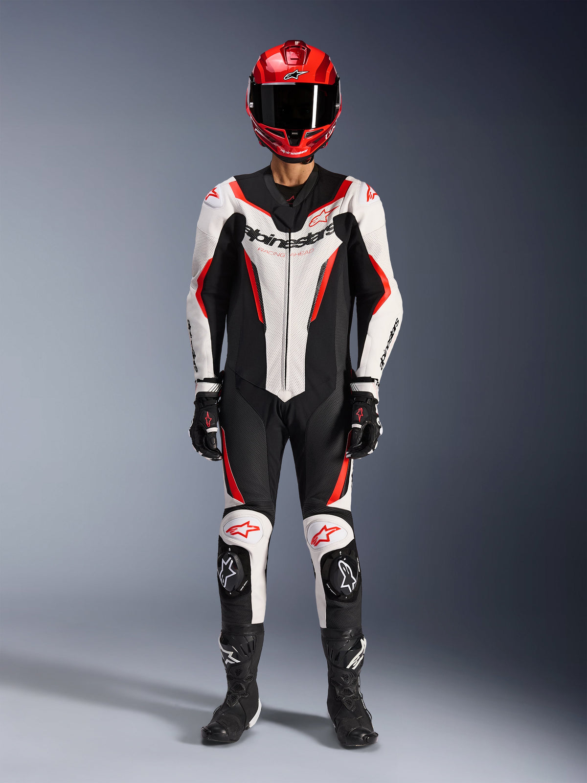 Mono de cuero Alpinestars GP Force V2 de 1 pieza, blanco, negro y rojo flúor, equipamiento completo de carreras que incluye casco rojo, guantes y botas negros, con diseño aerodinámico y logotipos de Alpinestars en el pecho y las rodillas