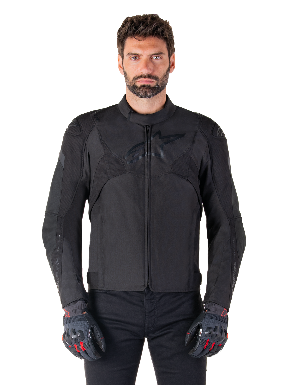 Chaqueta impermeable Alpinestars T-Jaws V4, chaqueta deportiva de moto negra, vestida por un hombre con guantes negros con detalles rojos, hombros y brazos reforzados, diseño estilizado con un logotipo sutil en el pecho, equipamiento textil de conducción para todo clima