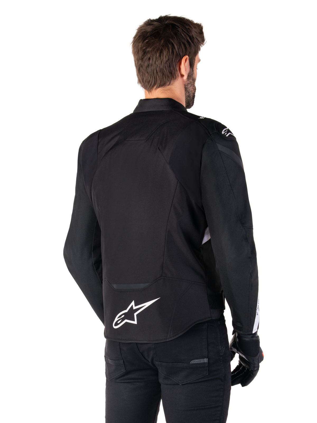 Chaqueta impermeable Alpinestars T-Jaws V4, negro y blanco, vista trasera, chaqueta textil deportiva para moto con logotipo blanco en la parte inferior de la espalda, combinada con guantes y pantalones negros, con una silueta de ajuste deportivo renovada