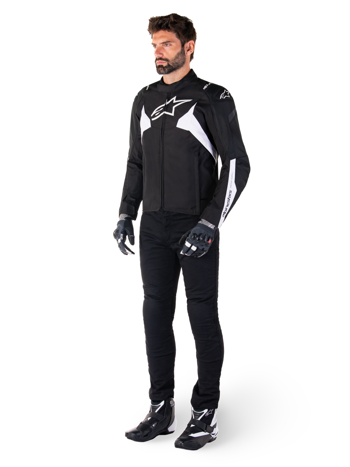 Chaqueta impermeable Alpinestars T-Jaws V4 en color negro y blanco, modelo masculino con chaqueta textil deportiva que incluye el logotipo de la estrella en blanco y detalles en las mangas, combinada con pantalones, guantes y botas de moto negros para un look completo de carretera.
