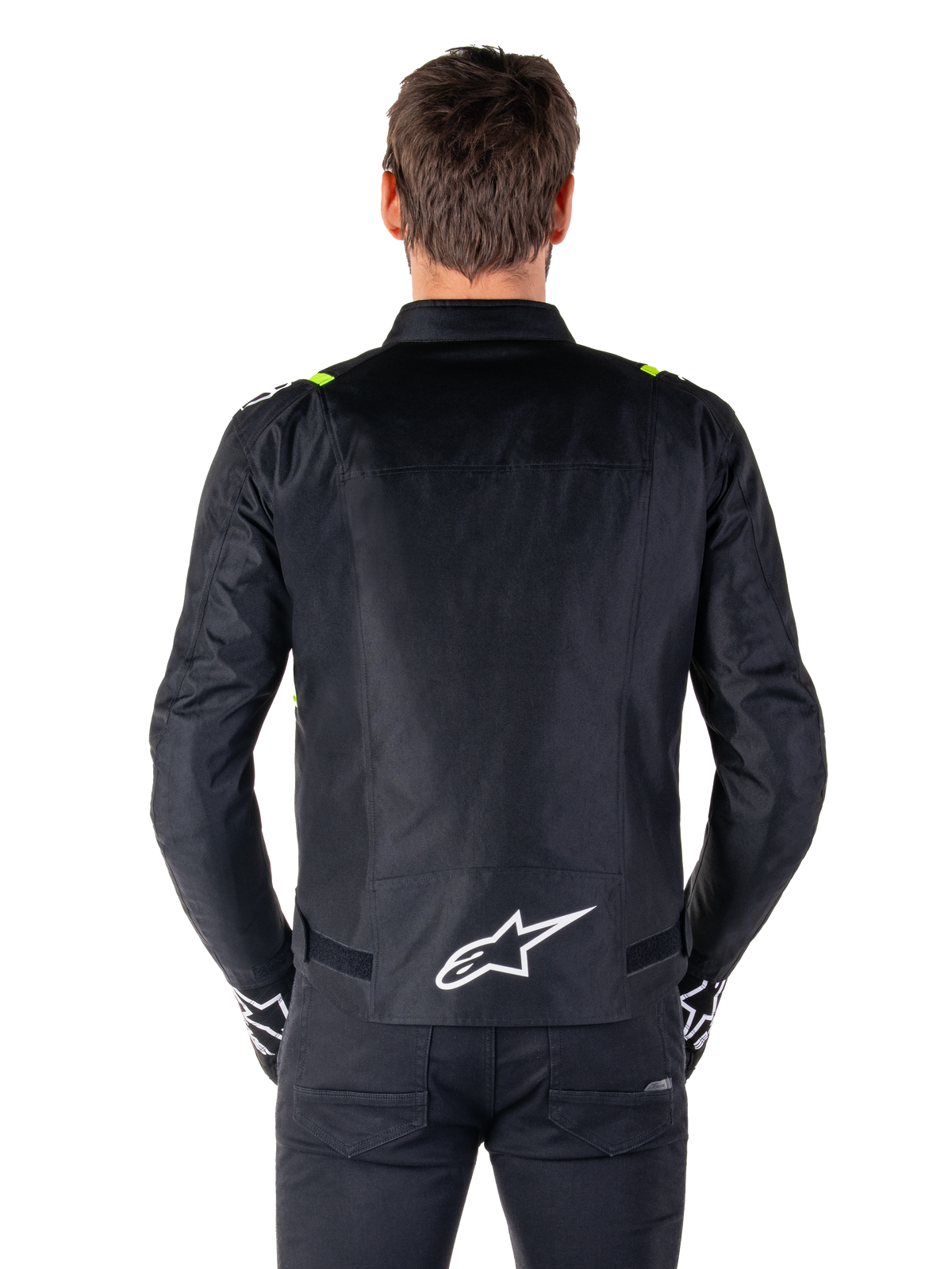 Chaqueta impermeable Alpinestars T-SPS V2, vista posterior, negra con detalles en amarillo flúor en los hombros y logotipo de estrella blanco en la parte inferior de la espalda, chaqueta de moto textil con silueta deportiva, usada por un modelo masculino.