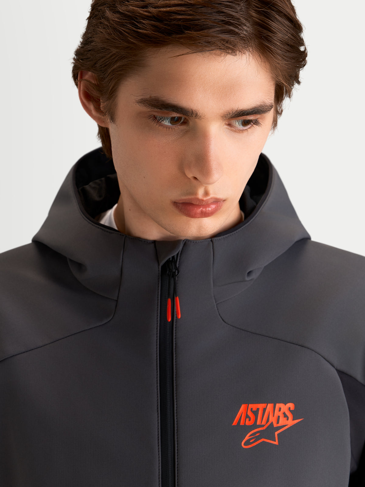 Alpinestars Aeroshell Wp Chaqueta, chaqueta de moto softshell para hombre en negro y gris oscuro, con capucha y detalle de logo ASTARS en naranja, primer plano en modelo.