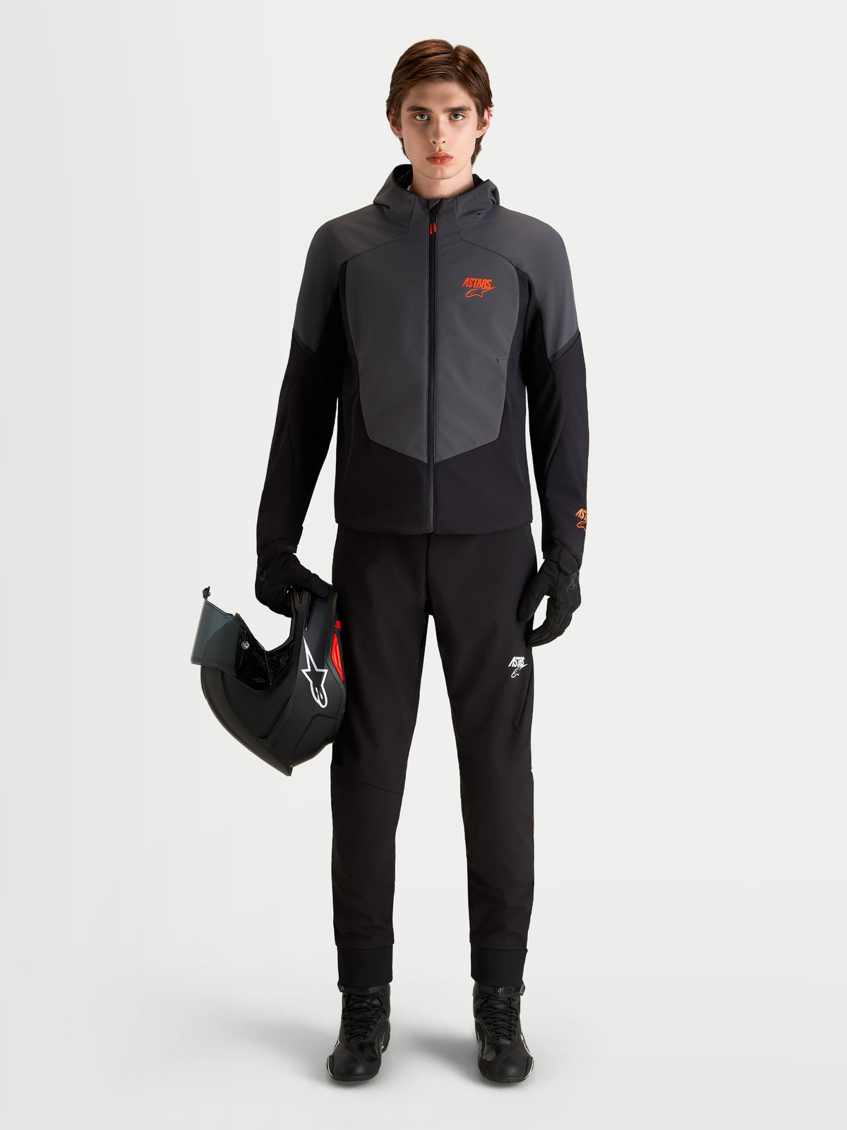 Alpinestars Aeroshell WP Chaqueta, chaqueta de moto impermeable para hombre en negro y gris oscuro, con capucha y protección con certificación CE, vestida por un modelo que sostiene un casco de moto