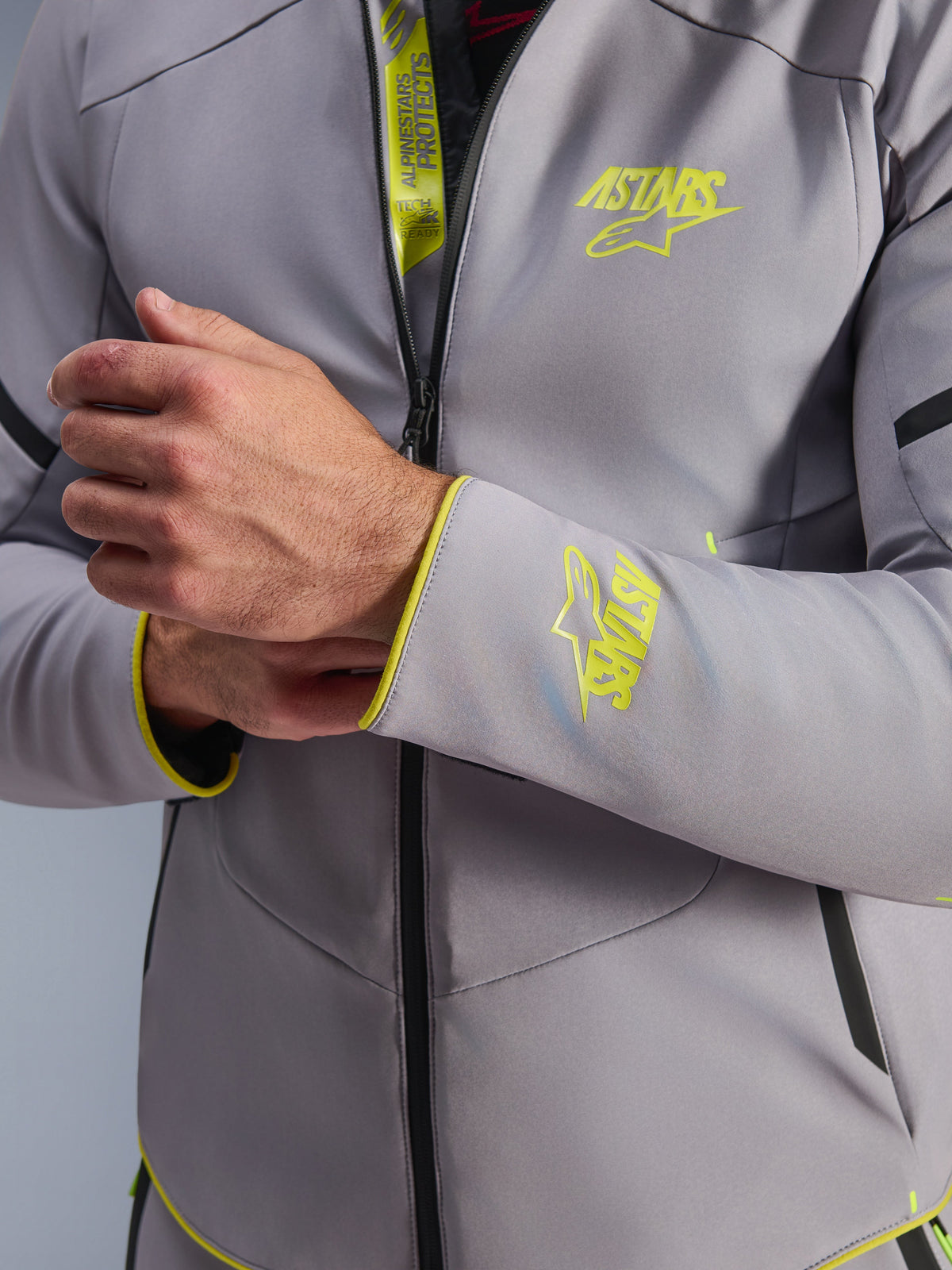 Chaqueta Alpinestars Aeroshell Waterproof, gris medio con detalles en amarillo flúor, primer plano del pecho y el puño de la manga que muestra los logotipos Astars en amarillo fluorescente, detalle de la solapa interna con la marca Tech-Air Ready, chaqueta de moto softshell deportiva moderna