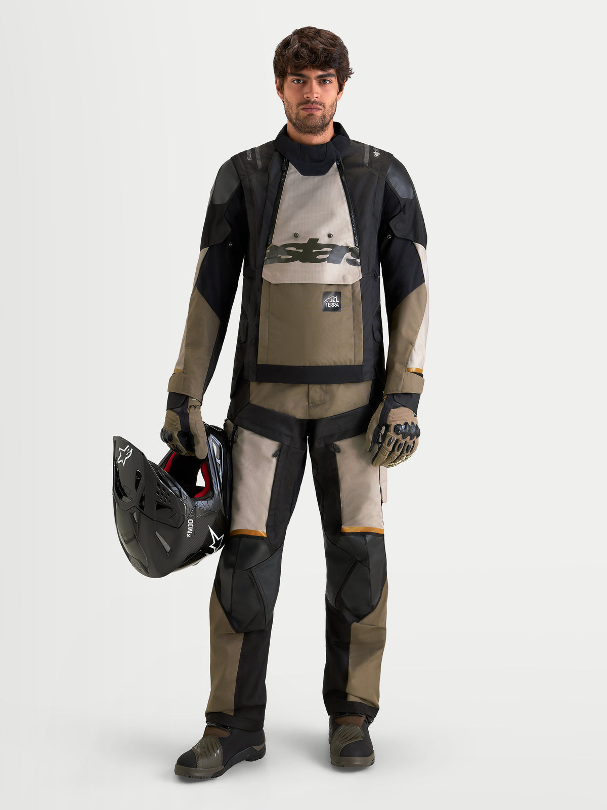 Chaqueta Alpinestars Harok V2 Drystar, chaqueta de moto para adventure all-terrain de hombre en aluminio, marrón y negro, vestida con equipamiento de aventura a juego mientras sostiene un casco