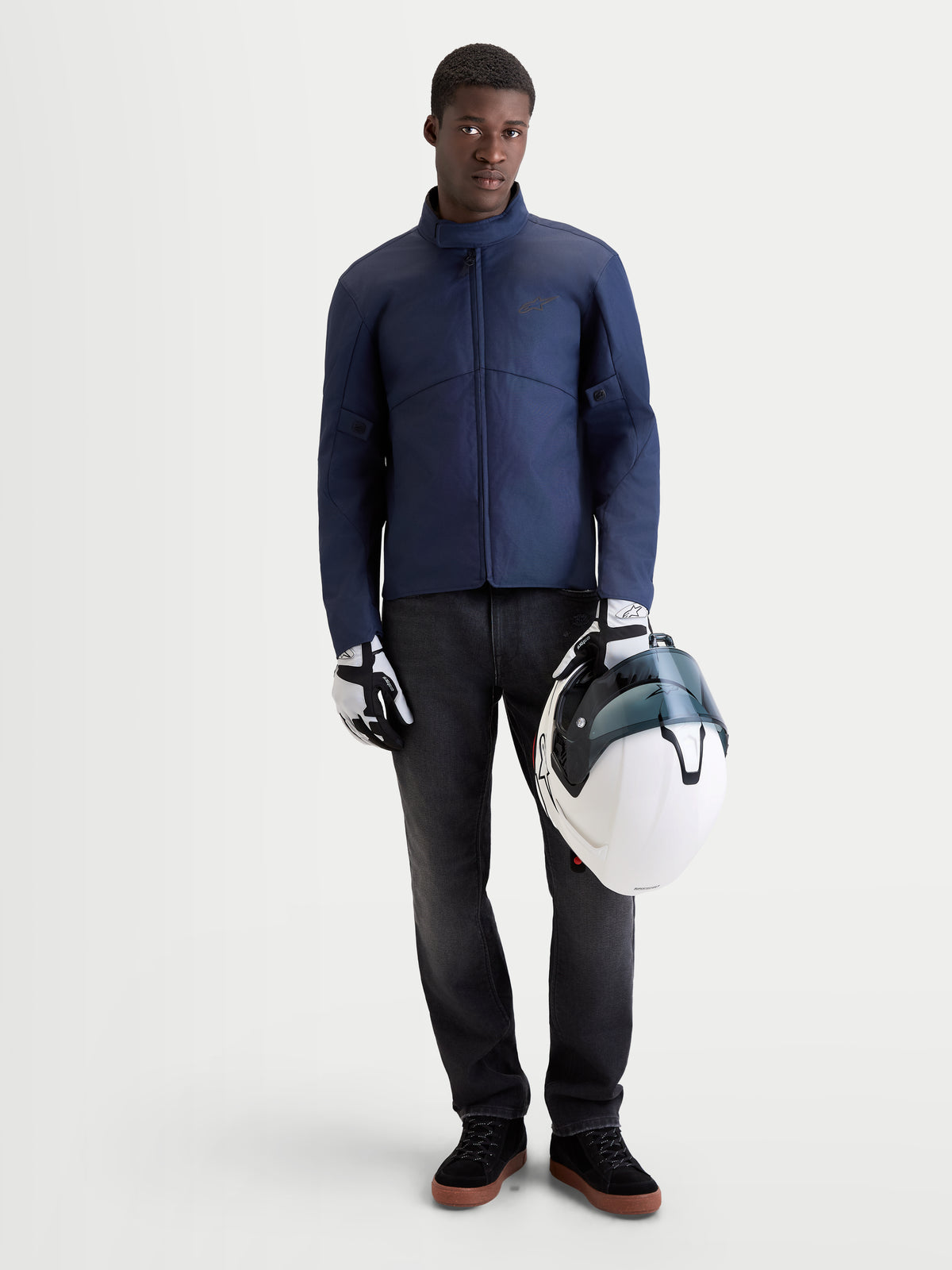 Alpinestars C-1 Waterproof Jacket, men's urban contemporary motorcycle textile jacket in dark blue, front view on a model wearing matching gloves and holding a white helmet, waterproof riding apparel for cold and wet conditions.