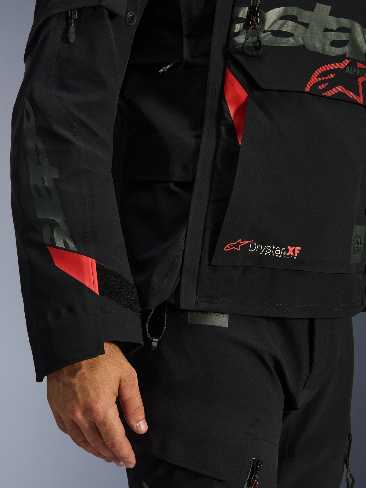 Chaqueta laminada Alpinestars Halo Pro Drystar® XF, chaqueta de moto, negra con detalles en rojo, primer plano con el logotipo Drystar® XF, textura técnica laminada y detalles ajustables en la manga para conducción de aventura
