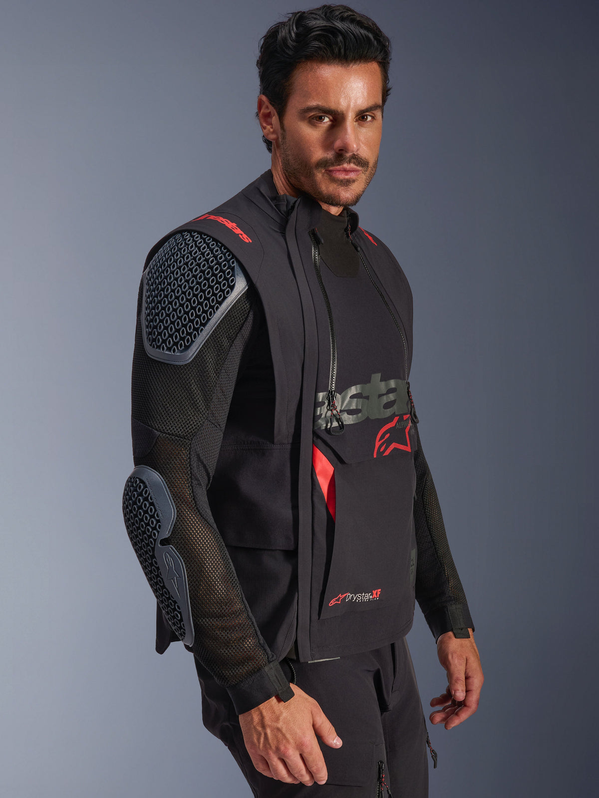 Chaqueta laminada Alpinestars Halo Pro Drystar® XF, negro y Dark Shadow, chaqueta de moto de aventura llevada por un modelo, configuración modular con mangas de malla y protecciones integradas en hombros y codos, acentos del logo en rojo y cremalleras impermeables técnicas.