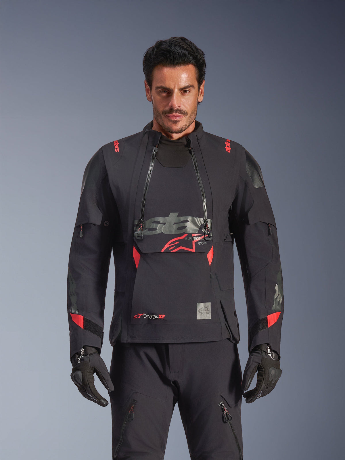 Alpinestars Halo Pro Drystar® XF Laminated Jacket, chaqueta de moto de aventura, color negro Dark Shadow con detalles en rojo, modelo masculino con equipamiento técnico completo incluyendo guantes y pantalones a juego, vista frontal destacando los paneles modulares de ventilación en el pecho y la construcción impermeable.