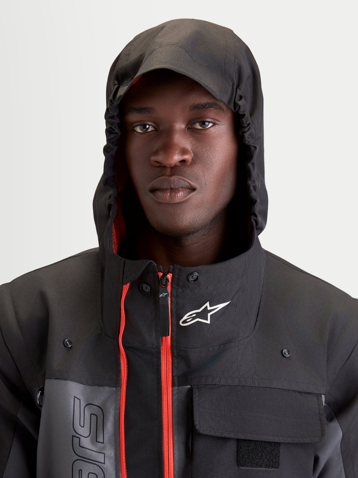 Alpinestars Morfex Parka Waterproof Jacket, men's urban contemporary motorcycle jacket in lunar gray and black, close-up portrait of a model wearing the jacket with integrated hood up and red interior accents visible