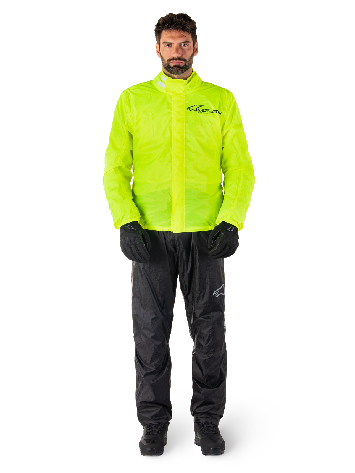 Chaqueta y pantalones Alpinestars Hurricane Rain V2, amarillo neón y negro, traje de lluvia impermeable para motocicleta usado con guantes y botas negras, con el logotipo de Alpinestars en el pecho y la pierna
