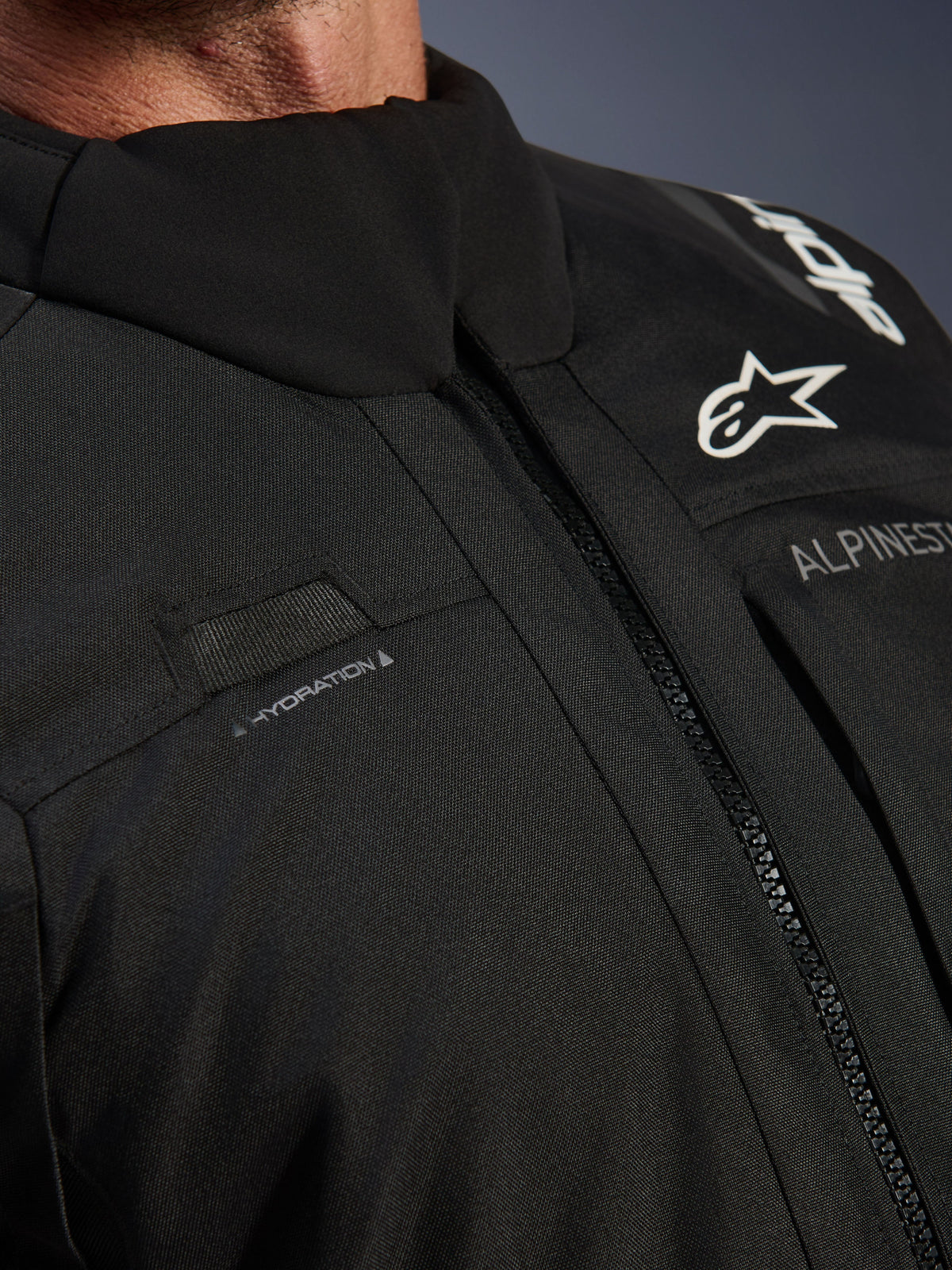 Alpinestars Andes V4 Drystar® Jacket, Black, close-up of chest detail featuring hydration hose loop, waterproof VISLON® front zipper, and Alpinestars logo on durable textile material