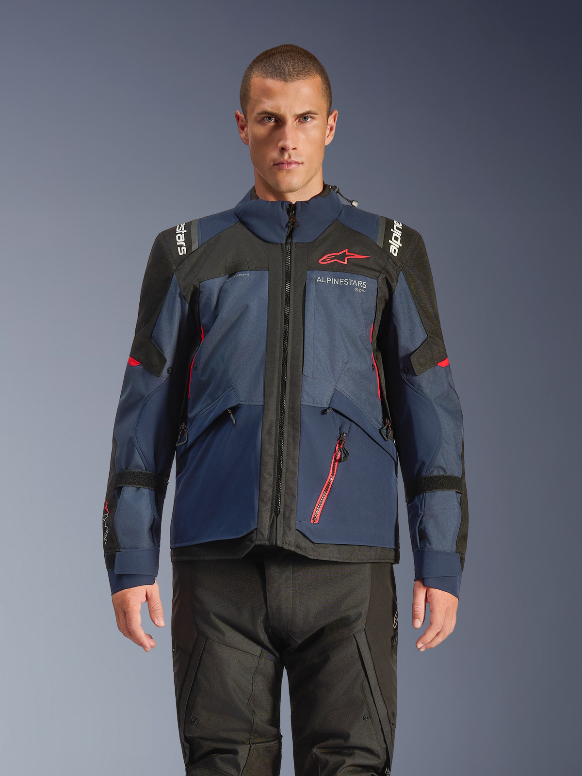 Chaqueta Alpinestars Andes V4 Drystar®, chaqueta de motociclismo de aventura, en azul noche y Mood Indigo con paneles negros, vestida por un modelo con pantalones de moto negros, logotipo de Alpinestars rojo en el pecho y detalle de cremallera roja, construcción textil resistente para touring en todo tipo de clima.