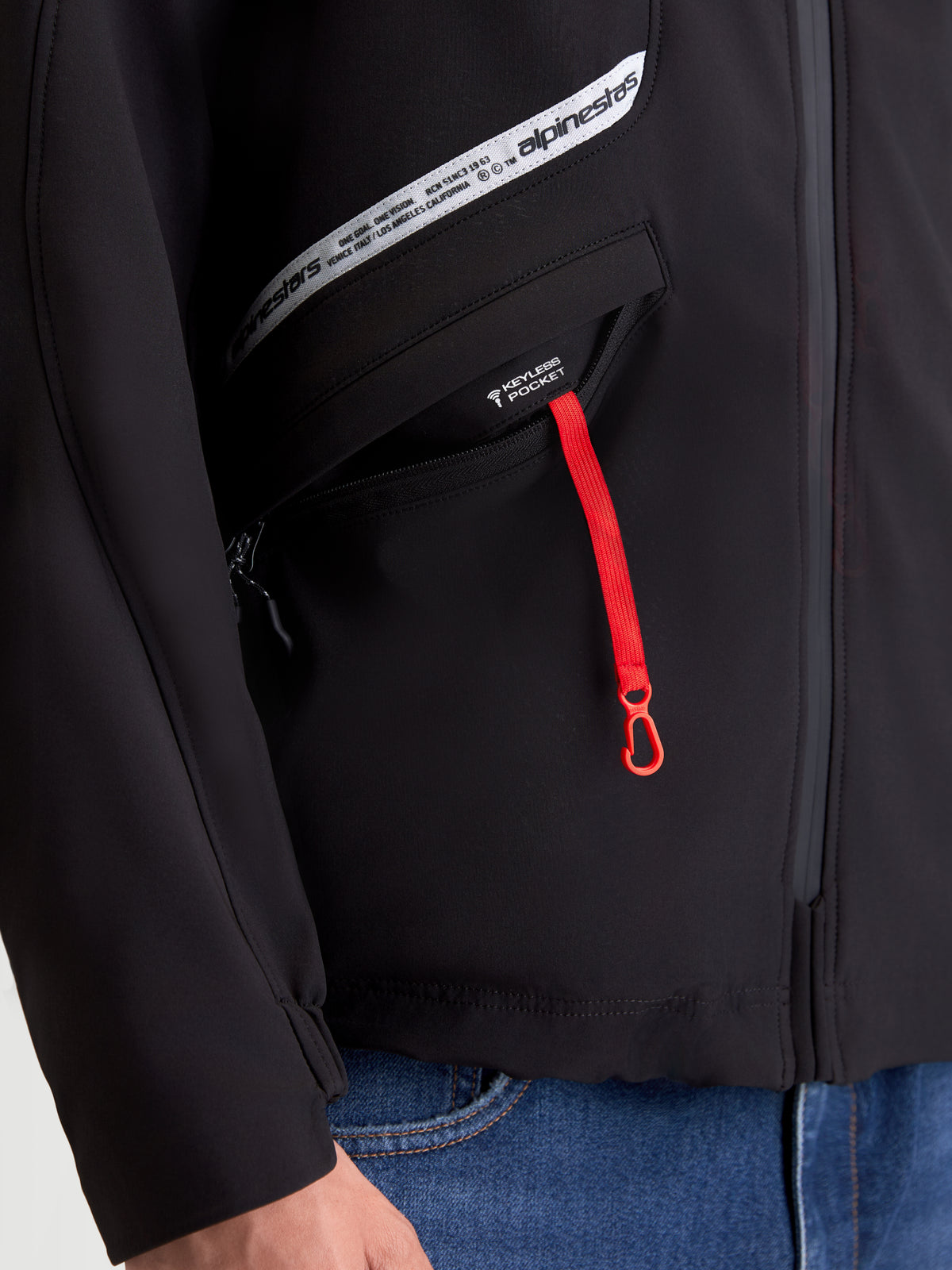 Alpinestars C 5 Drystar chaqueta de moto urbana, negra, vista en primer plano del bolsillo keyless con tirador de cremallera rojo y gráfico de la marca en el pecho