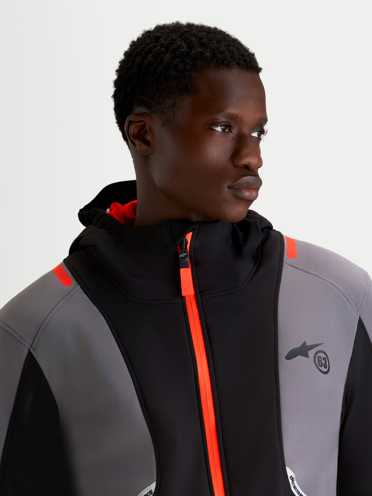Alpinestars C 5 Drystar Chaqueta, chaqueta de moto urbana para hombre en negro y gris oscuro, vista en primer plano de un modelo con la chaqueta softshell impermeable con cremallera frontal naranja brillante y capucha integrada