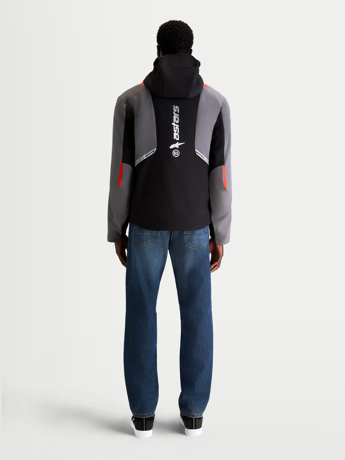 Alpinestars C 5 Drystar chaqueta, chaqueta de moto urbana contemporánea para hombre en negro y gris oscuro, vista trasera en un modelo con jeans, mostrando capucha integrada y gran logotipo vertical en la espalda