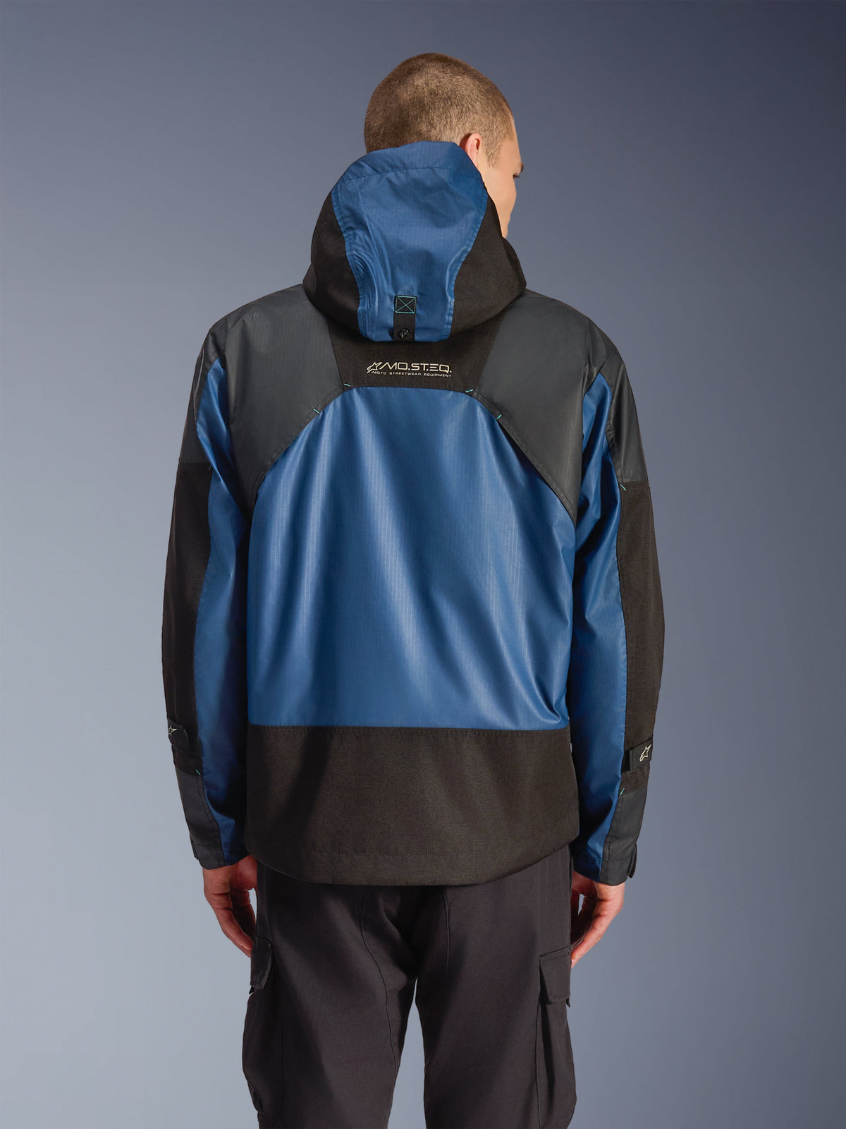 Chaqueta impermeable Alpinestars Mospher en Black Dark Petrol, vista trasera de una parka de moto con paneles ripstop azules y secciones reforzadas negras, logotipo MO.ST.EQ. en la parte superior de la espalda, diseño táctico urbano moderno