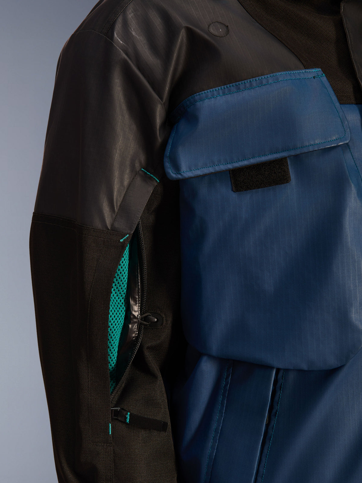 Primer plano de la chaqueta Alpinestars Mospher WP en negro y Dark Petrol, con una cremallera de ventilación abierta en la manga con forro de malla turquesa brillante, bolsillo grande en el pecho y material textil ripstop duradero.