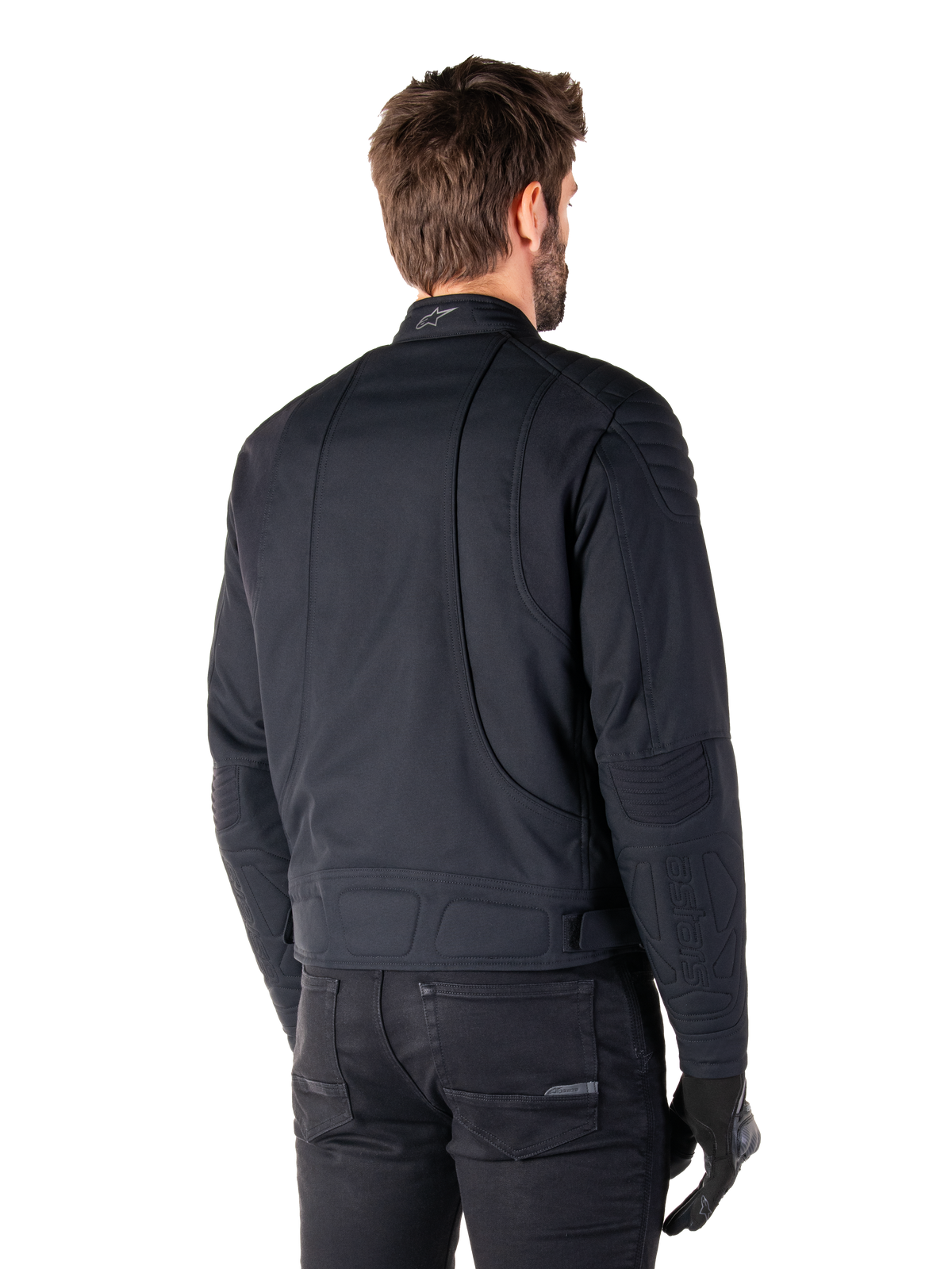 Chaqueta Alpinestars Clayton WR en negro, vista trasera de tres cuartos en un modelo masculino, chaqueta de moto urbana con acolchado en hombros y codos, líneas de costura técnicas y logotipo reflectante en el cuello, combinada con pantalones y guantes negros