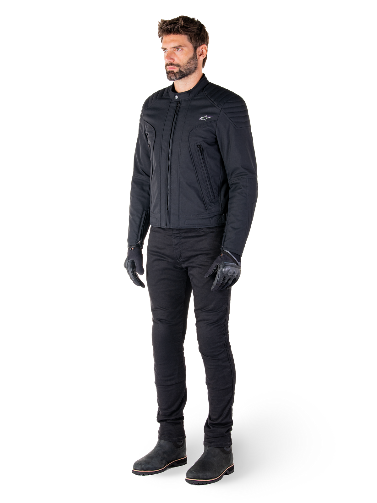 Piloto vistiendo la chaqueta Alpinestars Clayton WR, chaqueta de moto urbana negra, diseño ajustado con detalles acolchados en los hombros y acabado mate, combinada con pantalones técnicos de pilotaje y guantes negros.