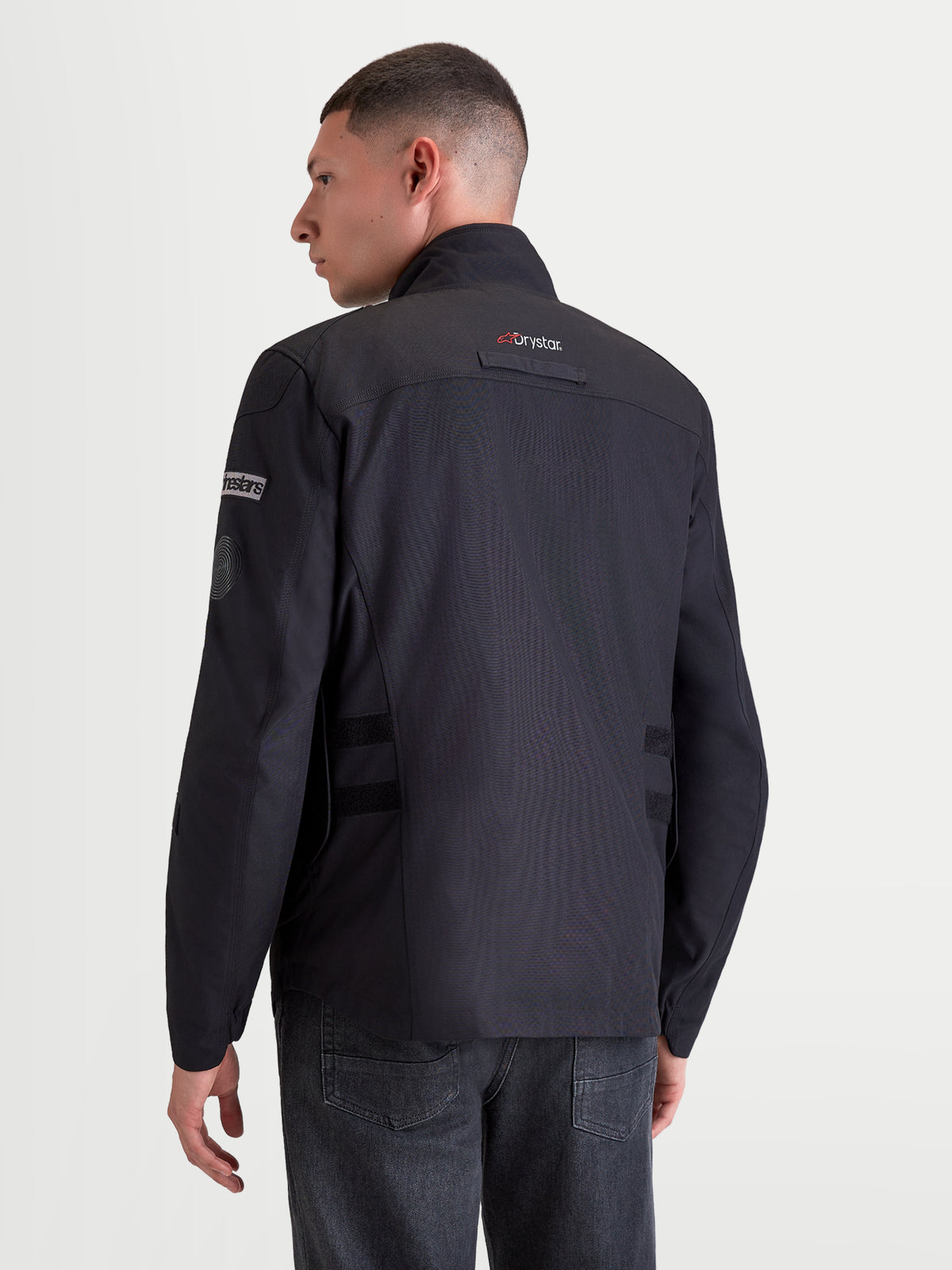 Alpinestars Altan Drystar Chaqueta, chaqueta de moto urbana contemporánea para hombre en negro, vista del perfil trasero en un modelo que lleva la chaqueta de equitación impermeable con tecnología Drystar y cuello cálido integrado