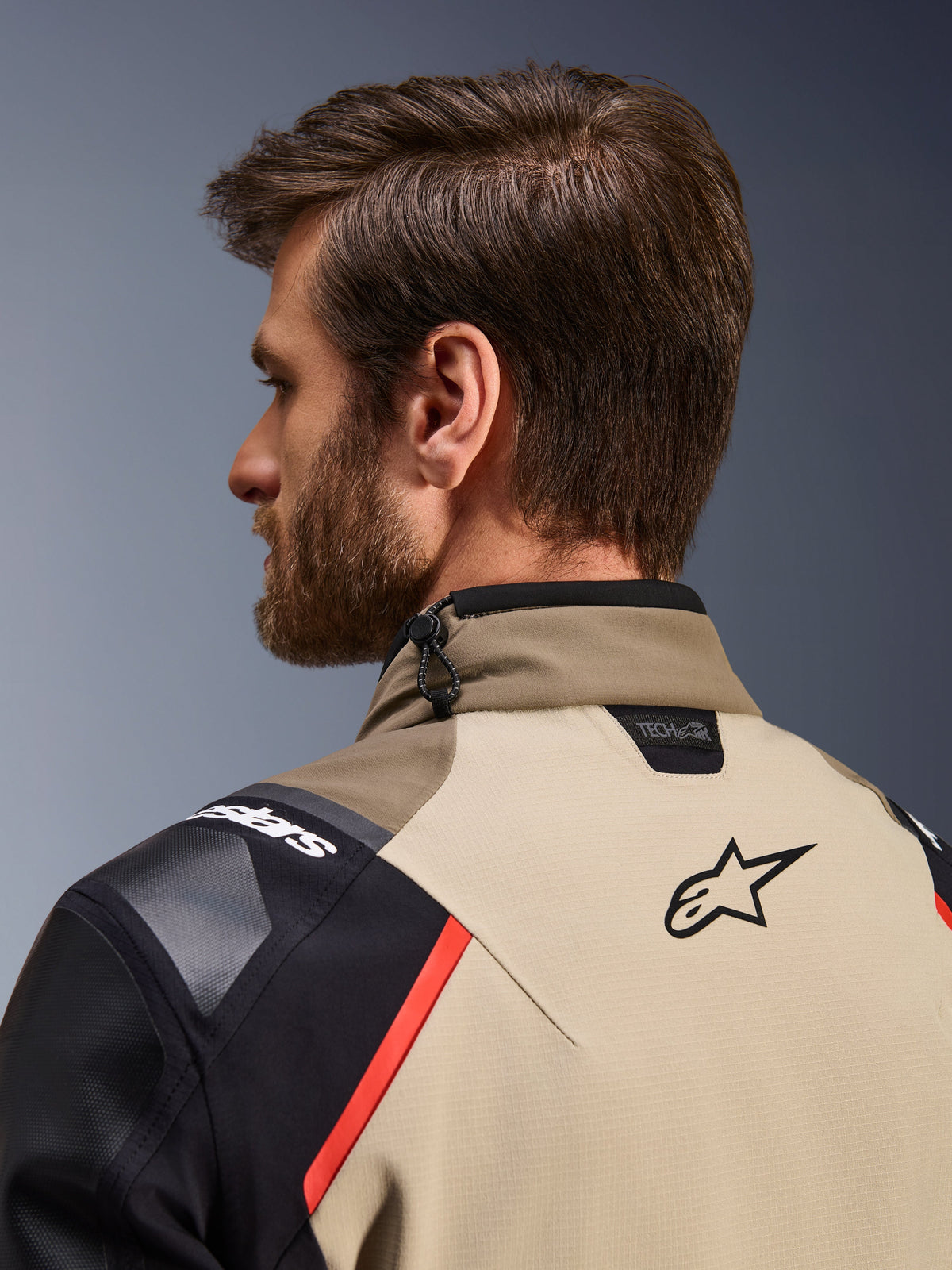 Chaqueta Alpinestars Andes Pro Drystar® XF en Walnut Aluminum, vista trasera en detalle del cuello y la parte superior de los hombros, con el logotipo de Alpinestars, marca de compatibilidad Tech-Air, detalles en rojo y sistema de ajuste mediante cordón elástico en el cuello.
