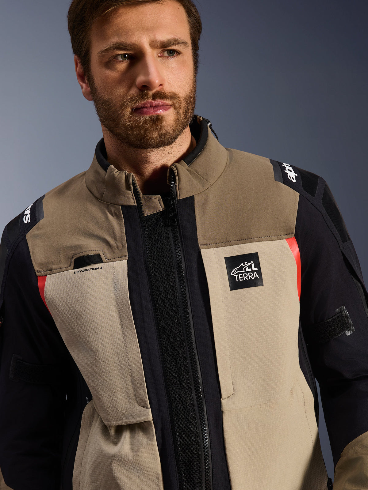 Chaqueta Alpinestars Andes Pro Drystar® XF en Walnut Aluminum, usada por un modelo masculino, chaqueta de motociclismo de aventura con diseño textil por capas en marrón, gris claro y negro con detalles en rojo, logo 'TERRA' de Alpinestars en el pecho y detalles técnicos visibles.