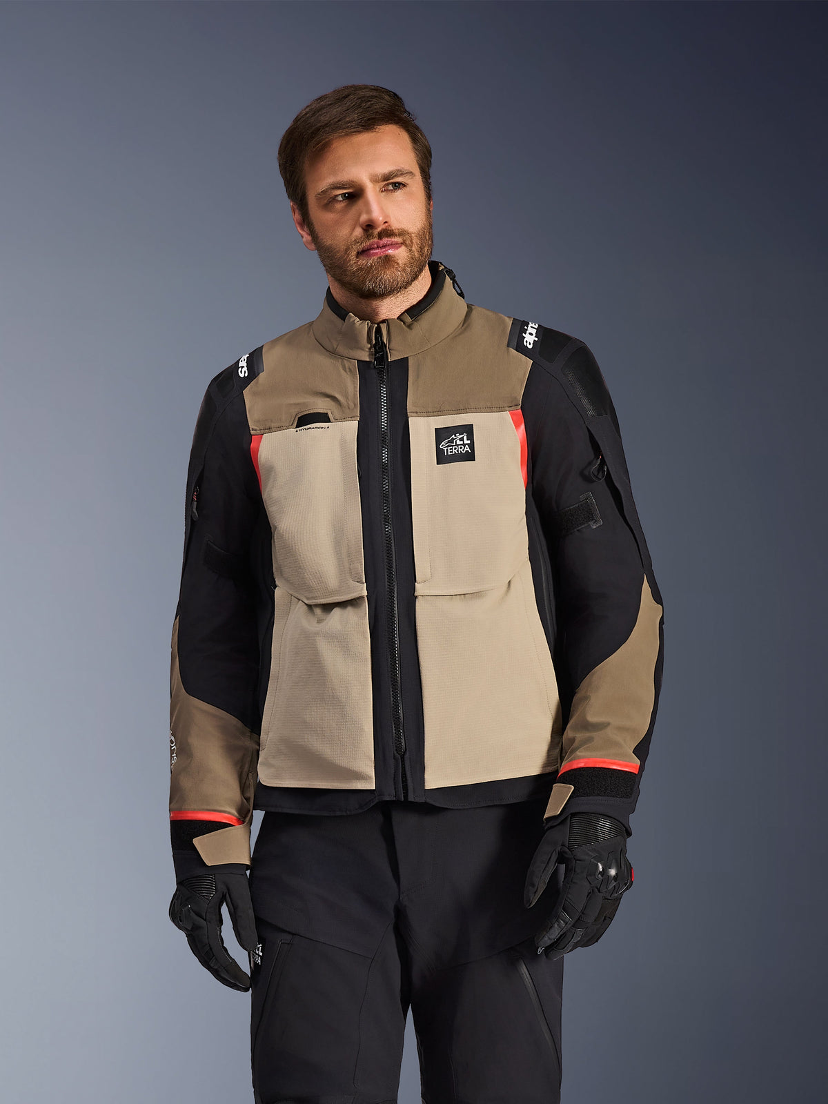 Chaqueta Alpinestars Andes Pro Drystar® XF, Walnut Aluminum, chaqueta de aventura para motocicleta con paneles en color tostado y negro con detalles rojos, usada con pantalones y guantes de motorista negros, equipamiento técnico de touring impermeable