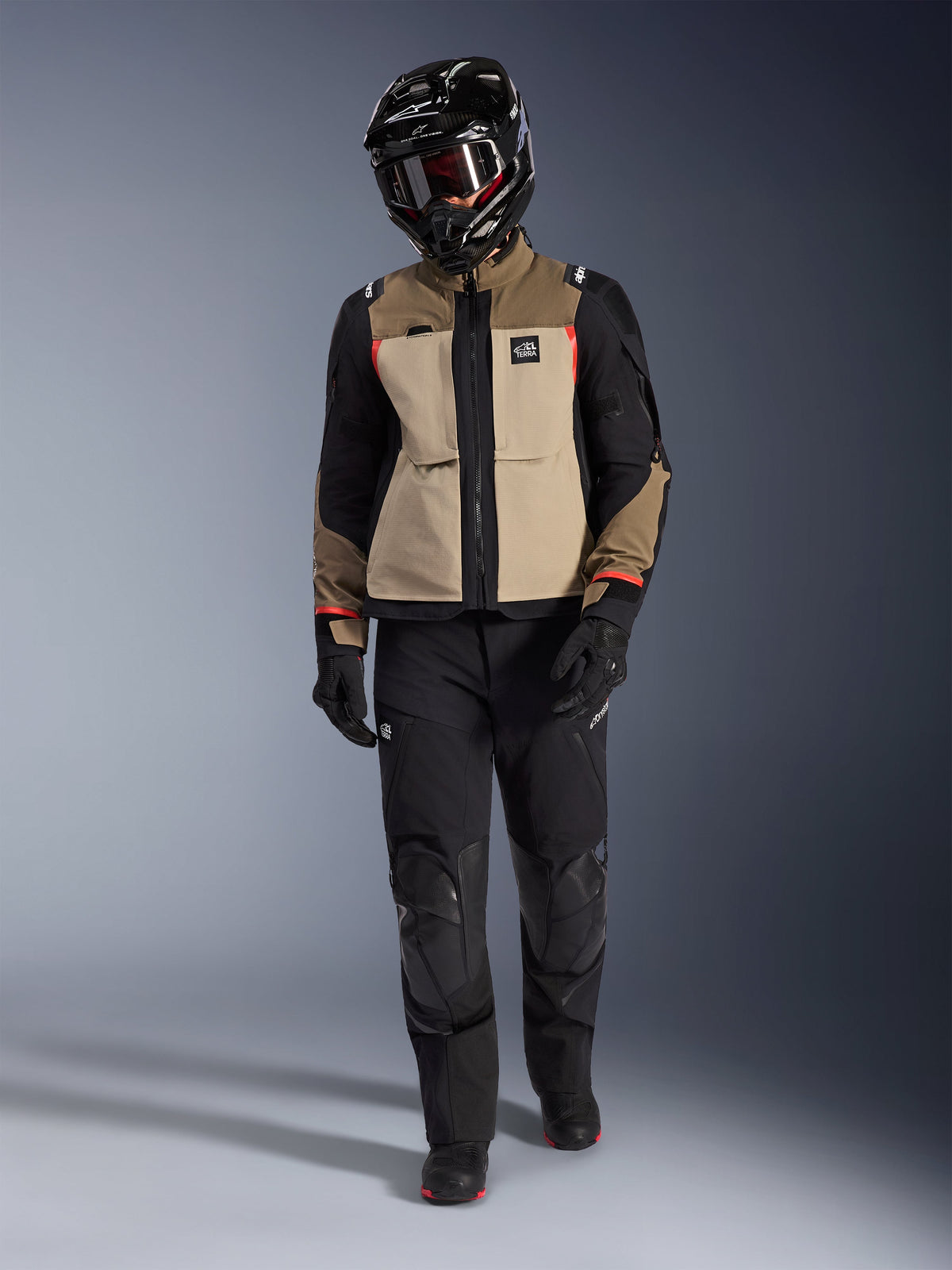 Chaqueta Alpinestars Andes Pro Drystar® XF en Walnut Aluminum, usada con pantalones de aventura negros, guantes negros y un casco integral negro con gafas, con detalles rojos y marca All Terra, equipamiento profesional para touring de aventura
