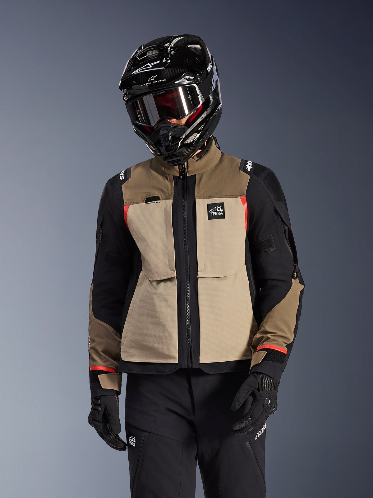 Chaqueta Alpinestars Andes Pro Drystar® XF, chaqueta de motociclismo Adventure Touring, color Walnut Aluminum beige y marrón con paneles negros y detalles rojos, usada con casco y gafas Alpinestars negros, equipamiento técnico de motociclismo para exteriores