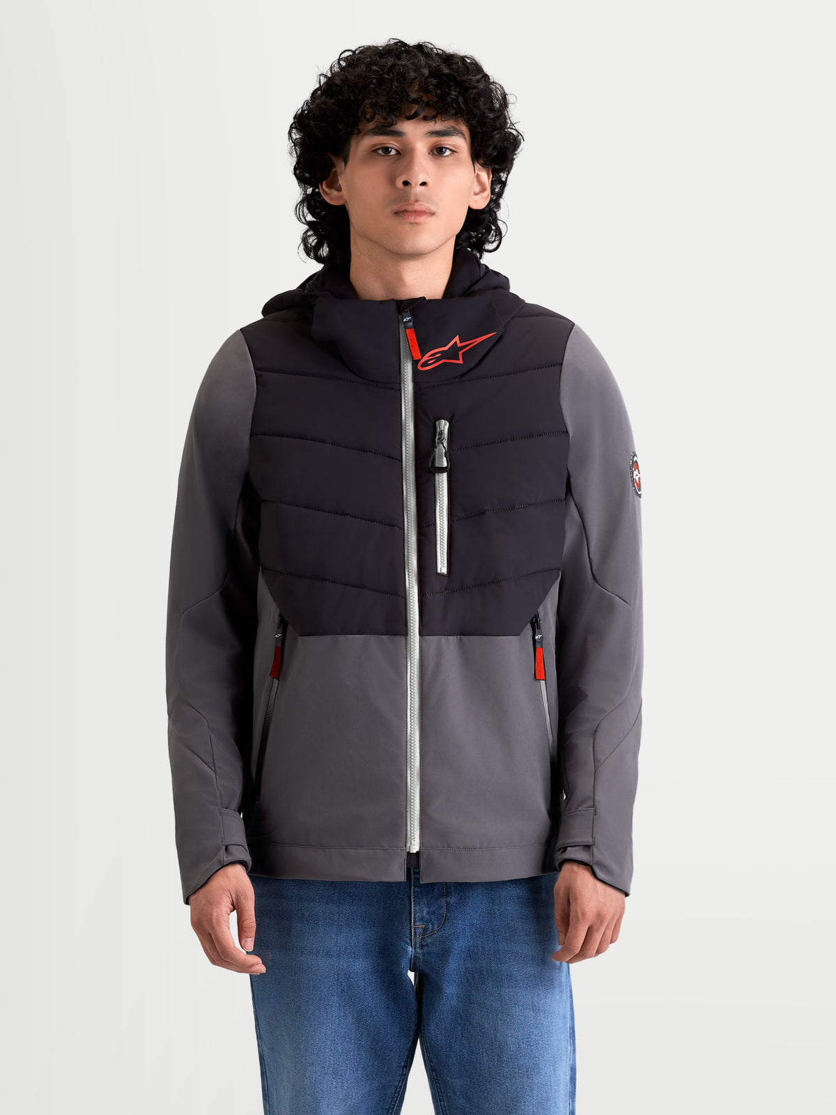 Chaqueta Therma-Tech Impermeable Alpinestars, chaqueta de moto urbana para hombre en color negro y gris oscuro, vista frontal en modelo con vaqueros, con construcción acolchada soldada por ultrasonidos, membrana impermeable y capucha integrada