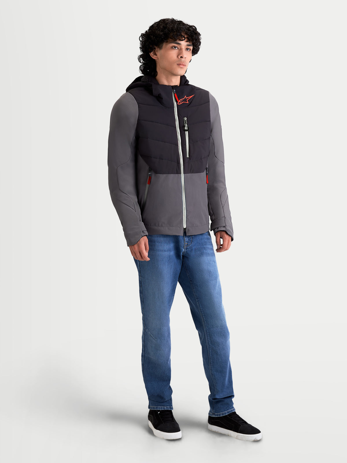 Alpinestars Chaqueta Therma-Tech Impermeable, chaqueta de moto urbana contemporánea para hombre, negra y gris oscuro, vista frontal de tres cuartos en modelo con sistema de capucha integrada y construcción acolchada termosellada