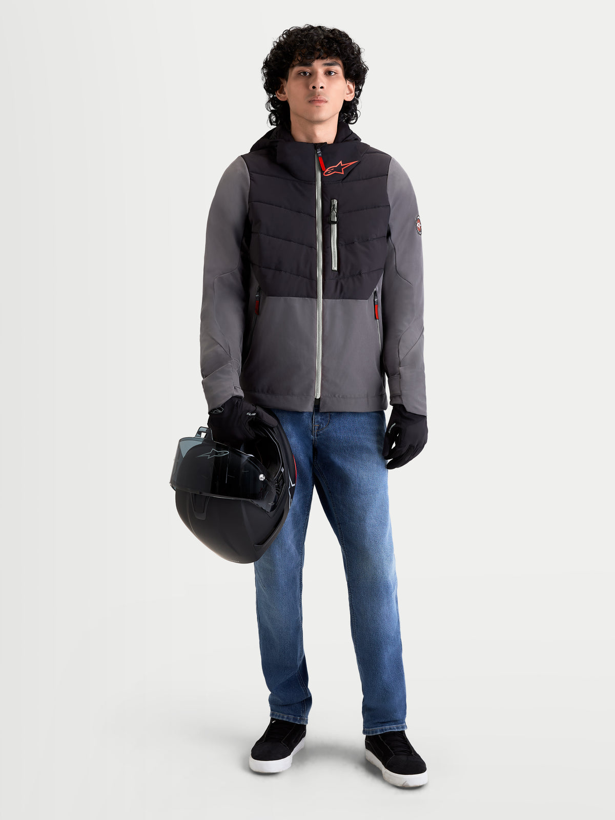 Alpinestars Chaqueta Therma-Tech Impermeable, chaqueta de moto urbana contemporánea para hombre, negra y gris oscuro, vista frontal en un modelo que lleva vaqueros, guantes y sostiene un casco