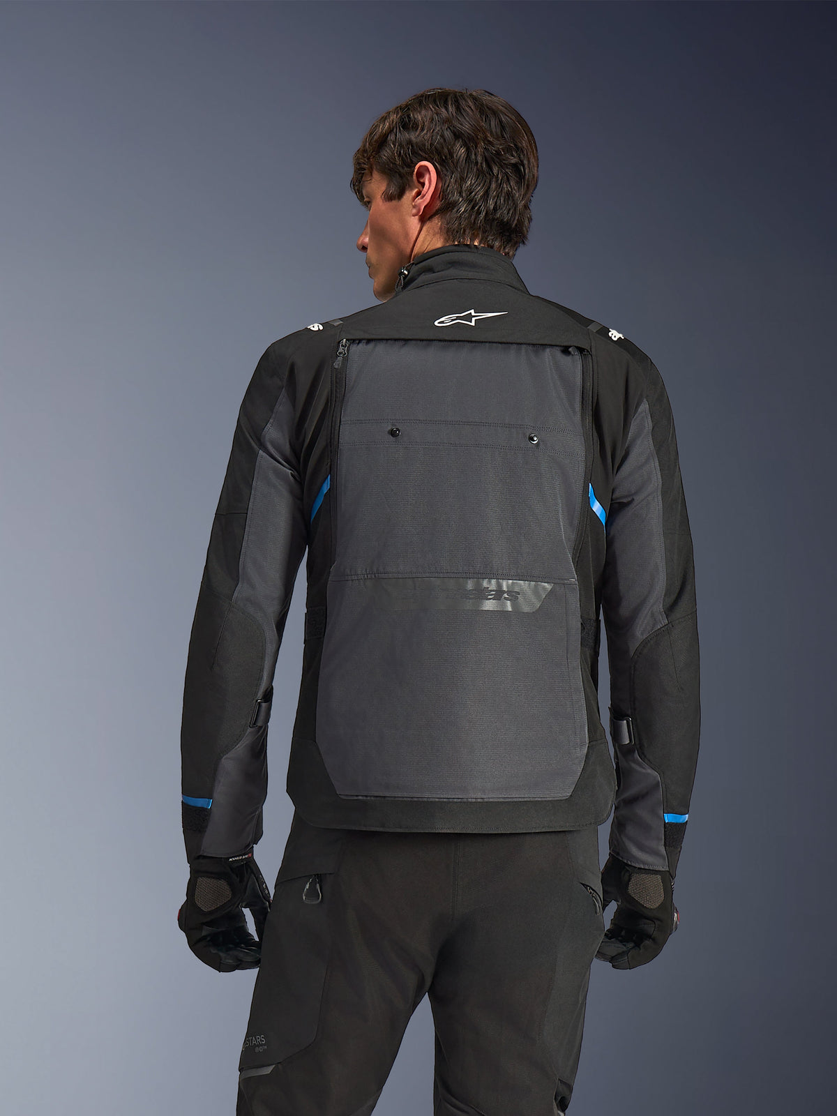 Chaqueta Alpinestars Cusco Drystar®, chaqueta de moto, negro y gris oscuro, vista posterior en un modelo que muestra un gran panel trasero gris, logotipo blanco de Alpinestars y detalles azules en las mangas.