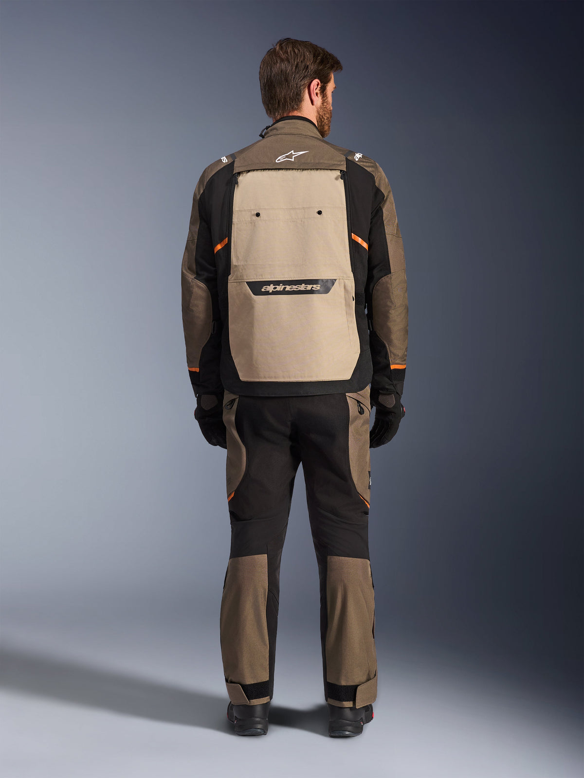 Chaqueta Alpinestars Cusco Drystar®, vista trasera, Walnut Aluminum Black, equipamiento textil para mototurismo de aventura, gran panel de ventilación trasero en color tostado con marca en negro, detalles en naranja, usada con pantalones y guantes a juego