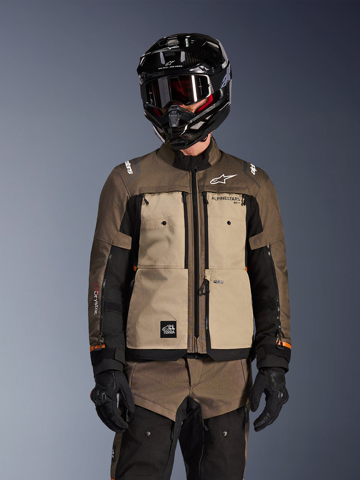 Piloto vistiendo la chaqueta Alpinestars Cusco Drystar en Walnut Aluminum Black, conjunto de motociclismo adventure touring con casco negro con gafas y guantes negros, vista frontal que muestra la construcción textil técnica, los bolsillos y la marca.