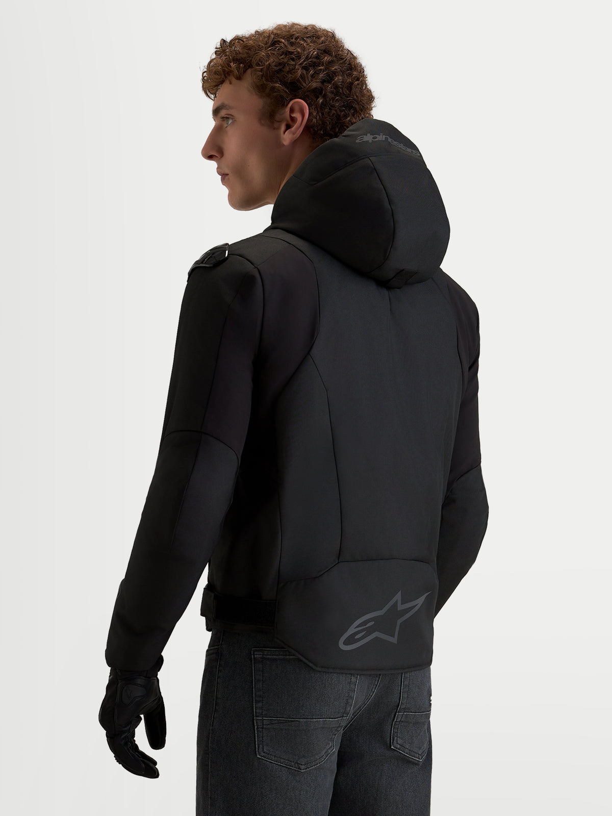 Alpinestars Zaca V 2 Waterproof Chaqueta, chaqueta de moto negra con capucha integrada y logo en el dobladillo trasero, vista trasera en modelo