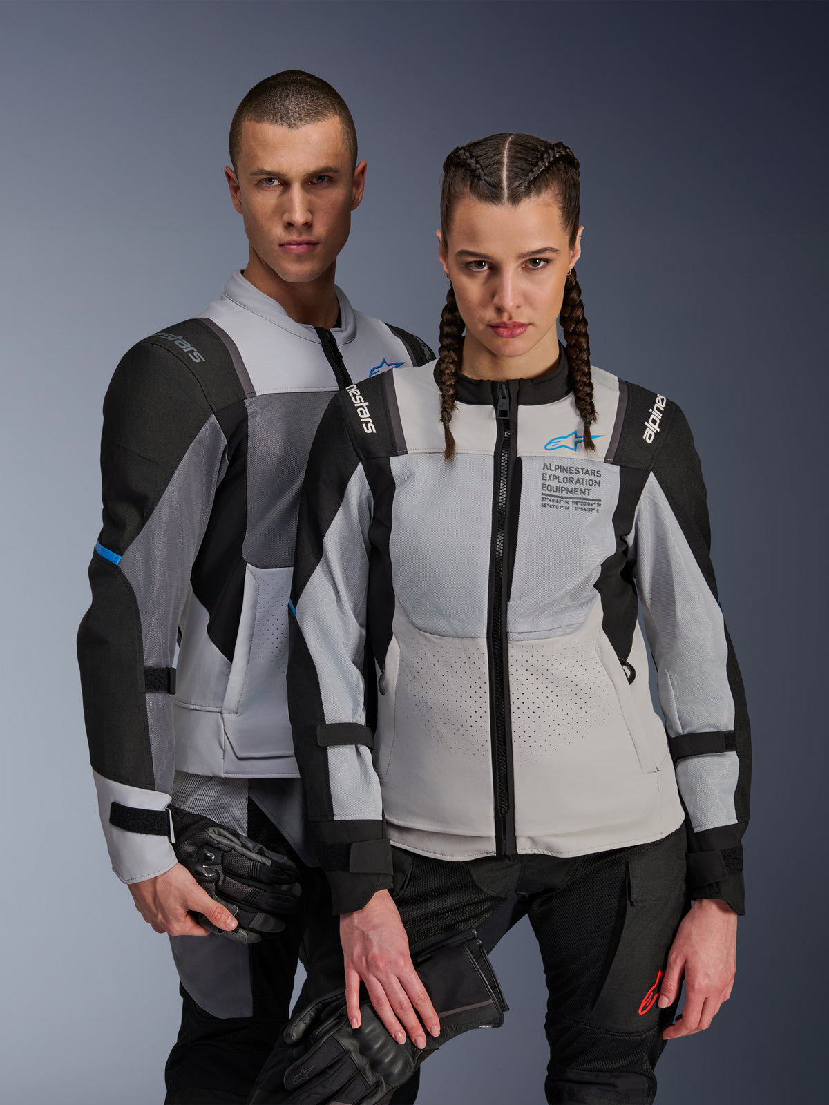 Alpinestars ST-2 Air Jackets, Textile Motorcycle Jackets, Ice Gray Dark Gray Black, couple wearing matching adventure touring gear with mesh ventilation panels and Alpinestars Exploration Equipment branding, holding motorcycle gloves