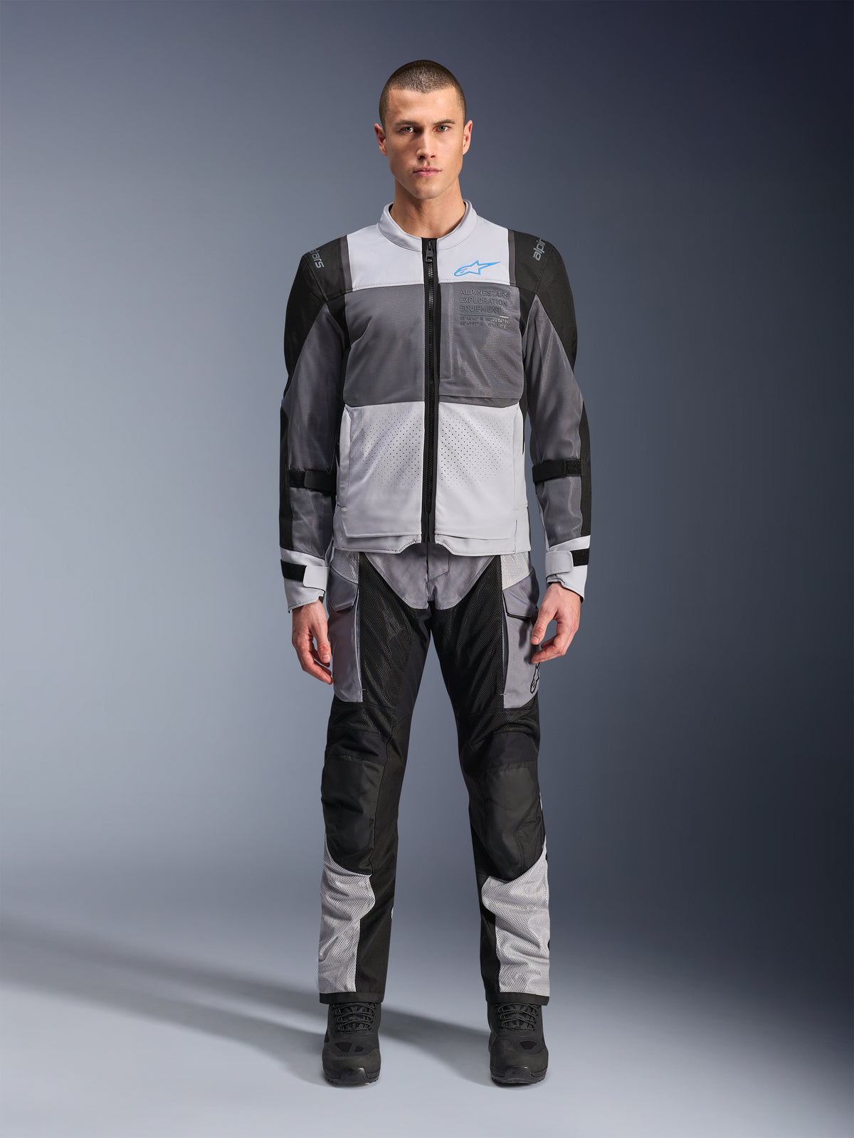 Alpinestars ST-2 Air Jacket, Motorcycle Touring Jacket, Ice Gray Dark Gray and Black, worn by a model with matching adventure pants, featuring large mesh panels, blue Alpinestars logo on chest, and Alpinestars Exploration Equipment branding.