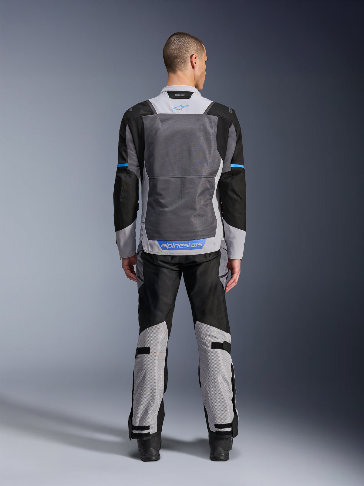 Alpinestars ST-2 Air Jacket, Ice Gray Dark Gray Black, rear view on model, featuring large mesh ventilation panels, blue accents and Alpinestars logo, paired with matching motorcycle pants for adventure touring.