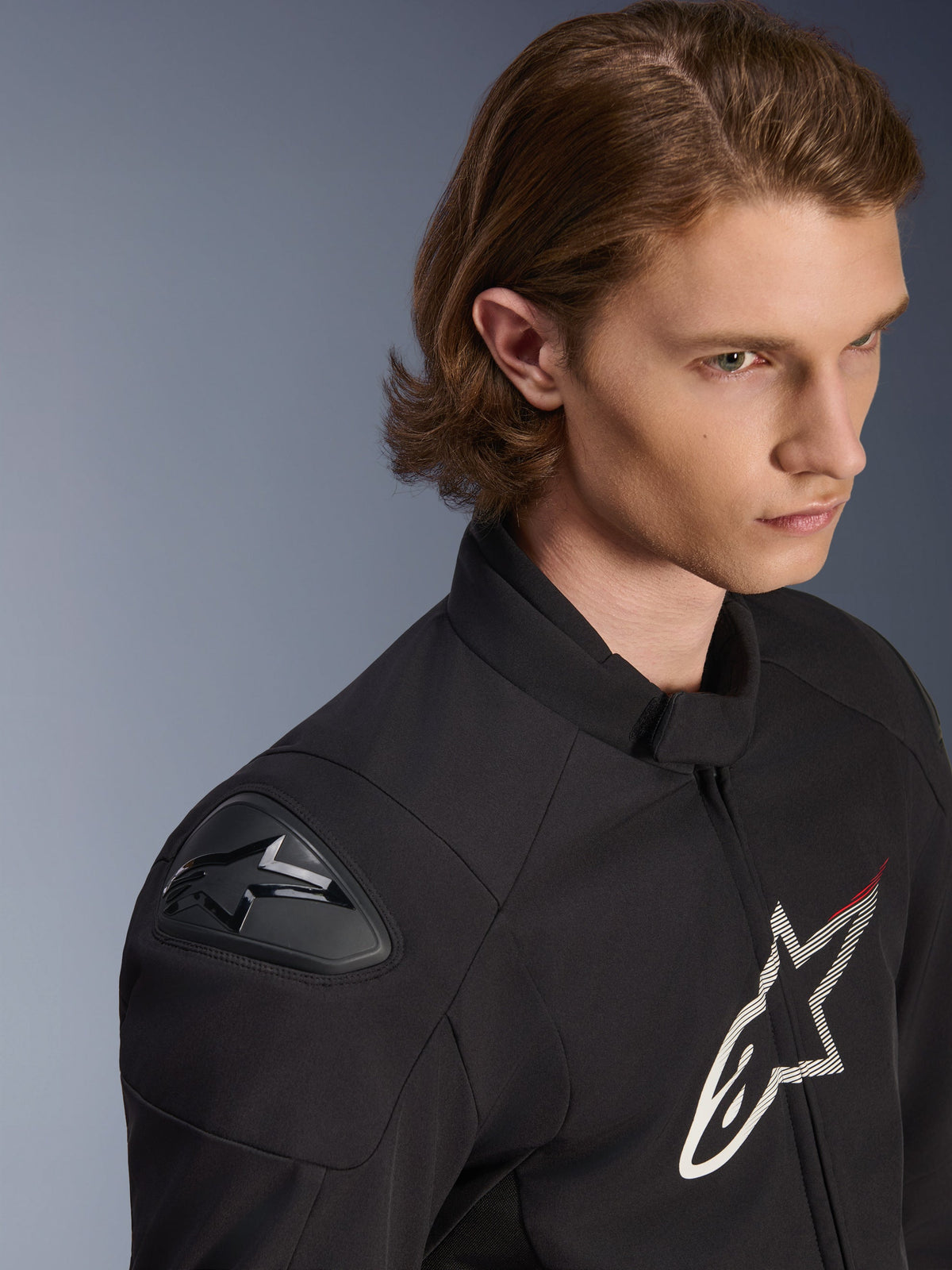 Chaqueta impermeable Alpinestars SMX, negra con detalles en blanco y rojo, primer plano de estilo de vida en un modelo masculino, con deslizadores de hombro externos DFS Lite y un gran logotipo de estrella en el pecho, equipamiento deportivo para motociclismo