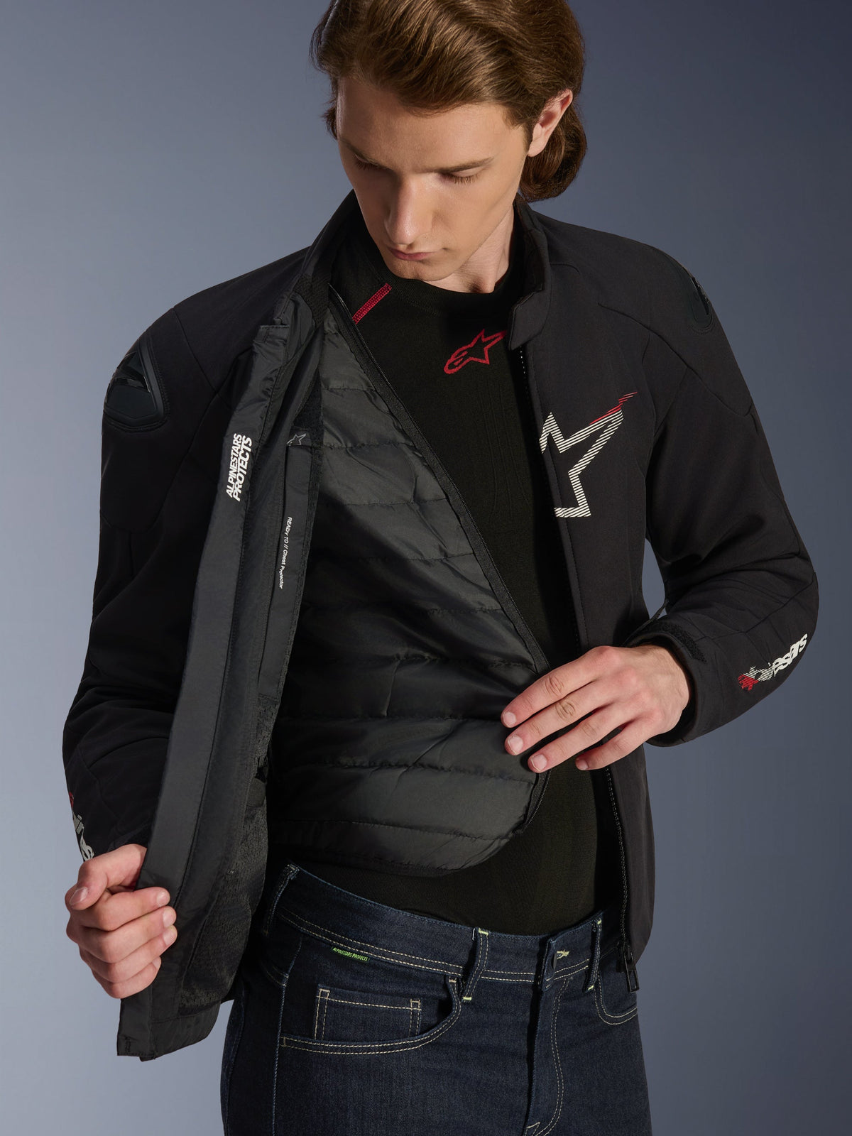 Chaqueta impermeable Alpinestars SMX en color negro, blanco y rojo brillante, usada por un hombre y abierta para mostrar el forro térmico acolchado desmontable, con hombros externos DFS lite y detalles de logotipos blancos, equipamiento de alto rendimiento para motociclismo de carretera