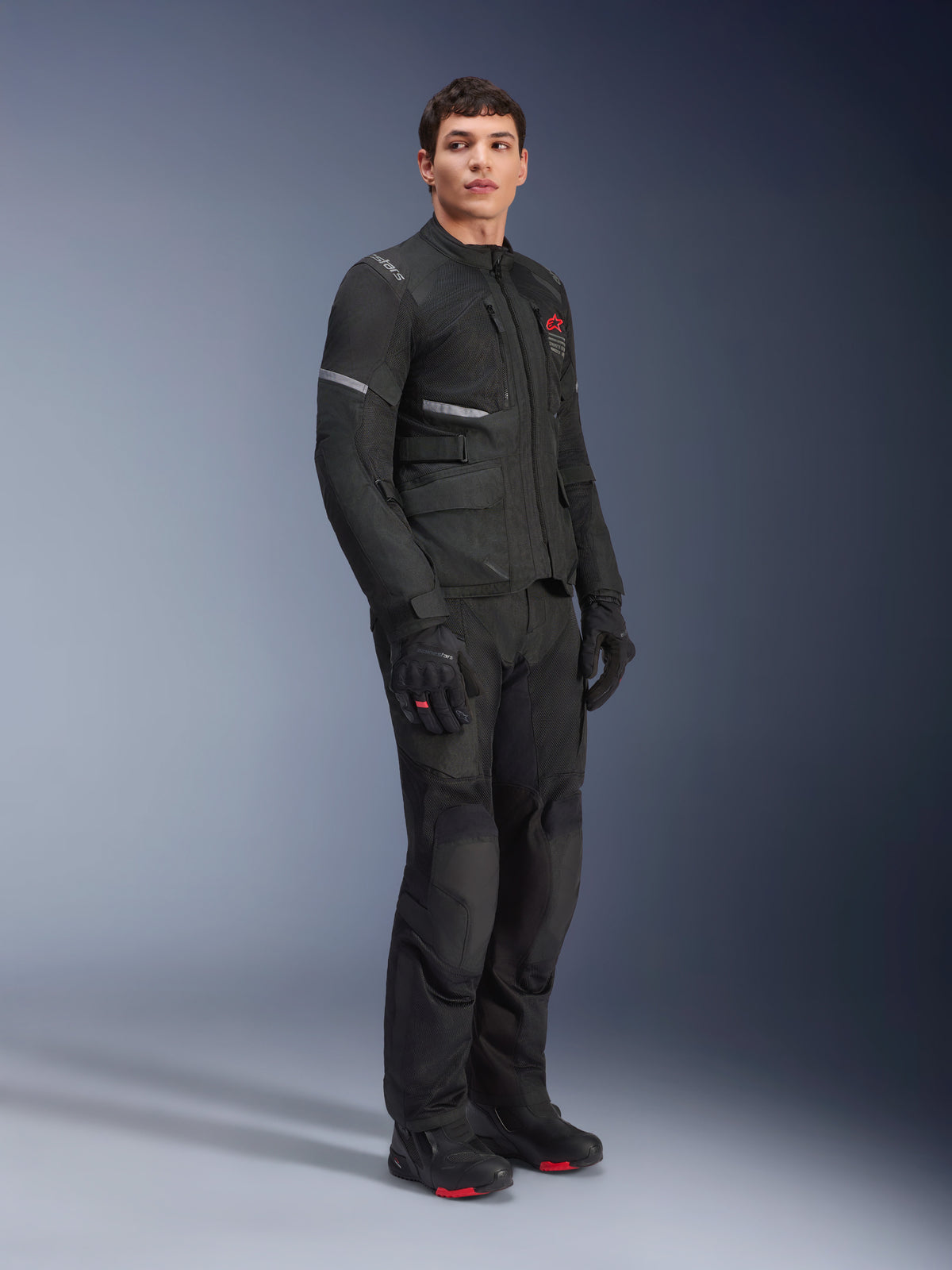 Alpinestars Andes Air Drystar® Jacket, Black, worn by a model as part of a full motorcycle adventure outfit with matching pants, gloves, and boots, featuring mesh ventilation panels, a red logo on the chest, and reflective strips for touring visibility.