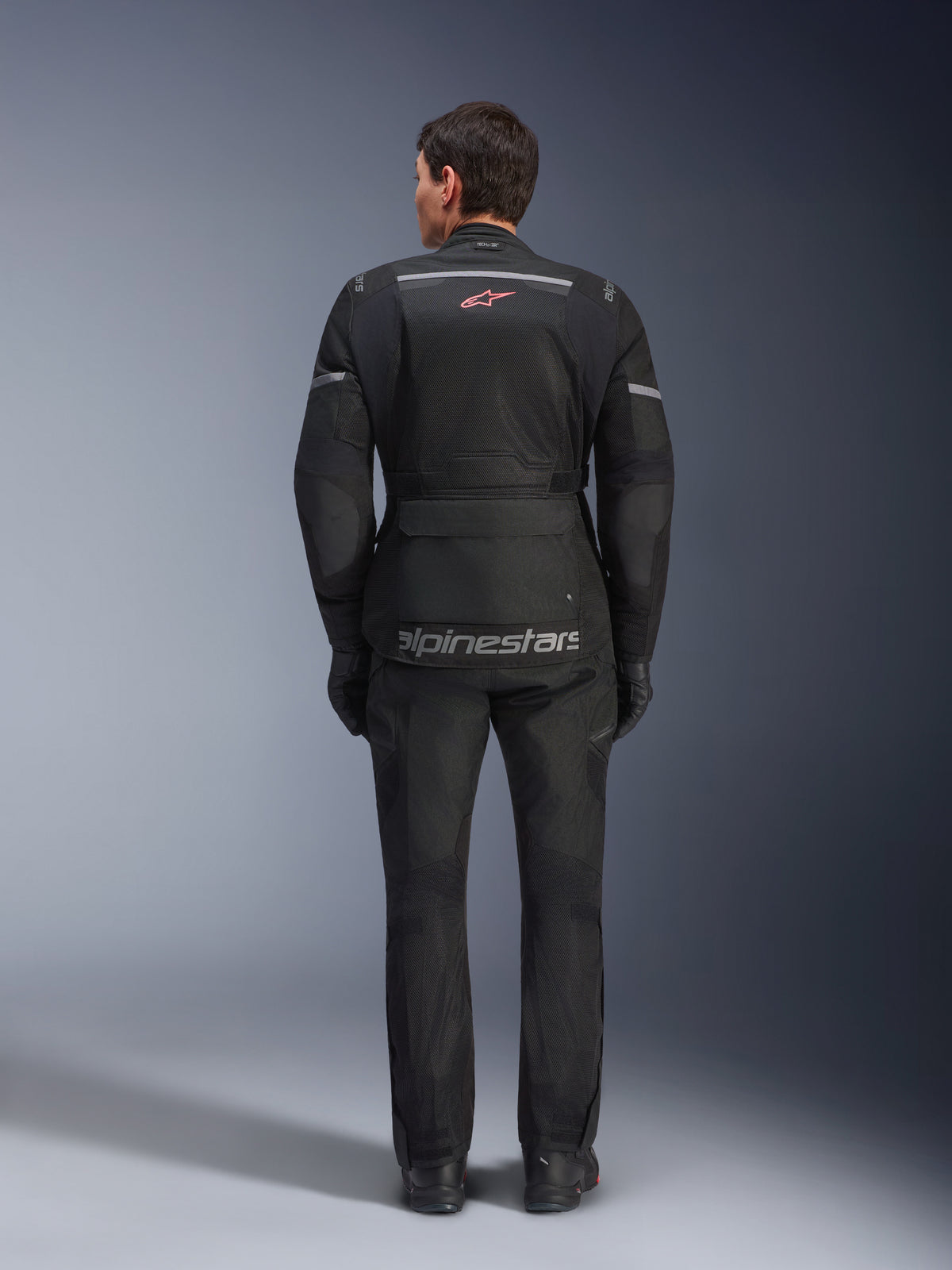 Chaqueta y pantalones Alpinestars Andes Air Drystar®, conjunto de motociclismo touring en negro, vista trasera del piloto, con paneles de malla, logotipo de estrella roja y marca reflectante Alpinestars en la chaqueta, combinado con guantes y botas negros