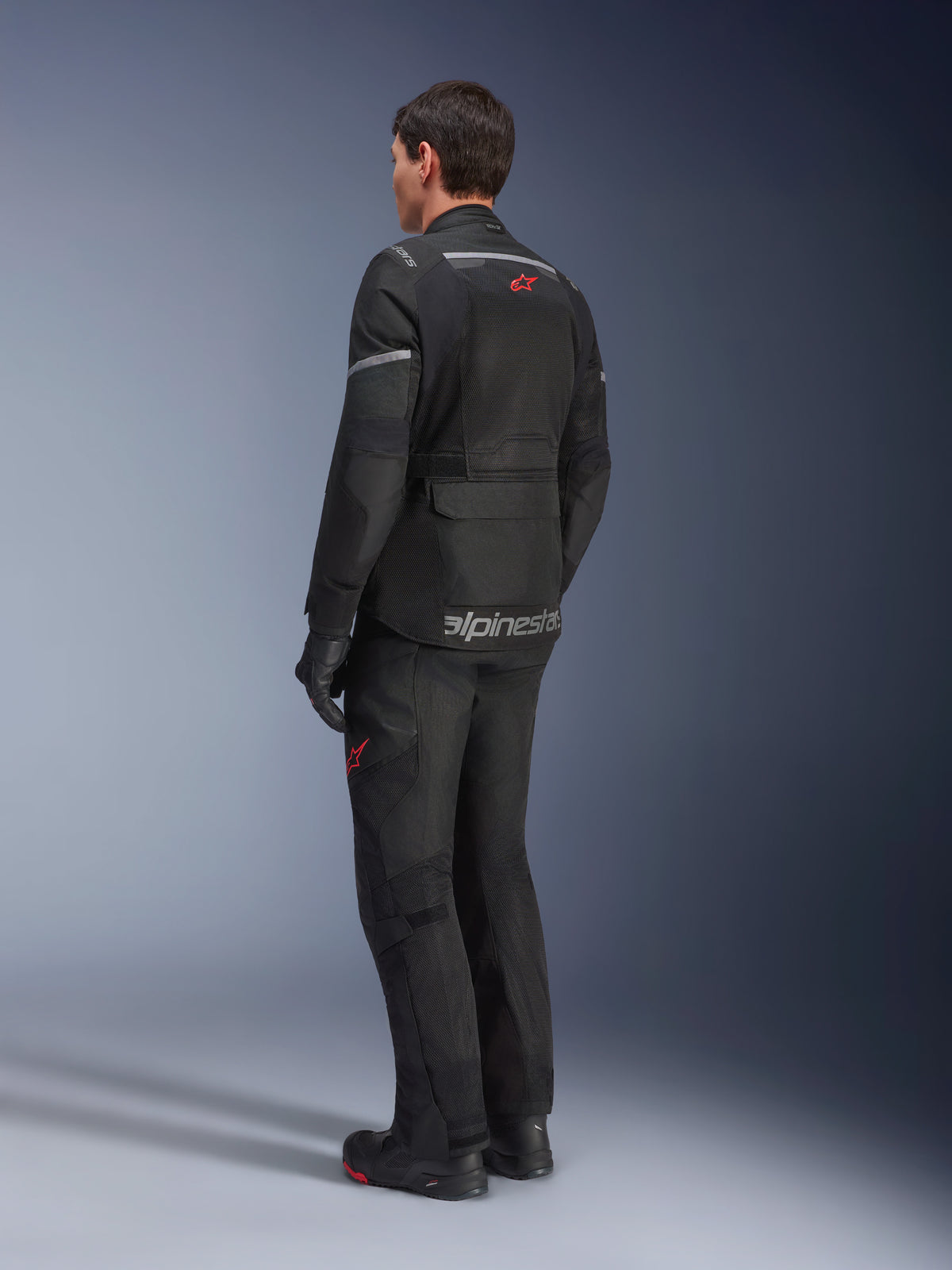 Pantalones Alpinestars Andes Air Drystar® y chaqueta a juego, negros con logotipos de estrella rojos, equipamiento de moto para aventura touring visto desde atrás, con paneles de ventilación de malla y detalles reflectantes.